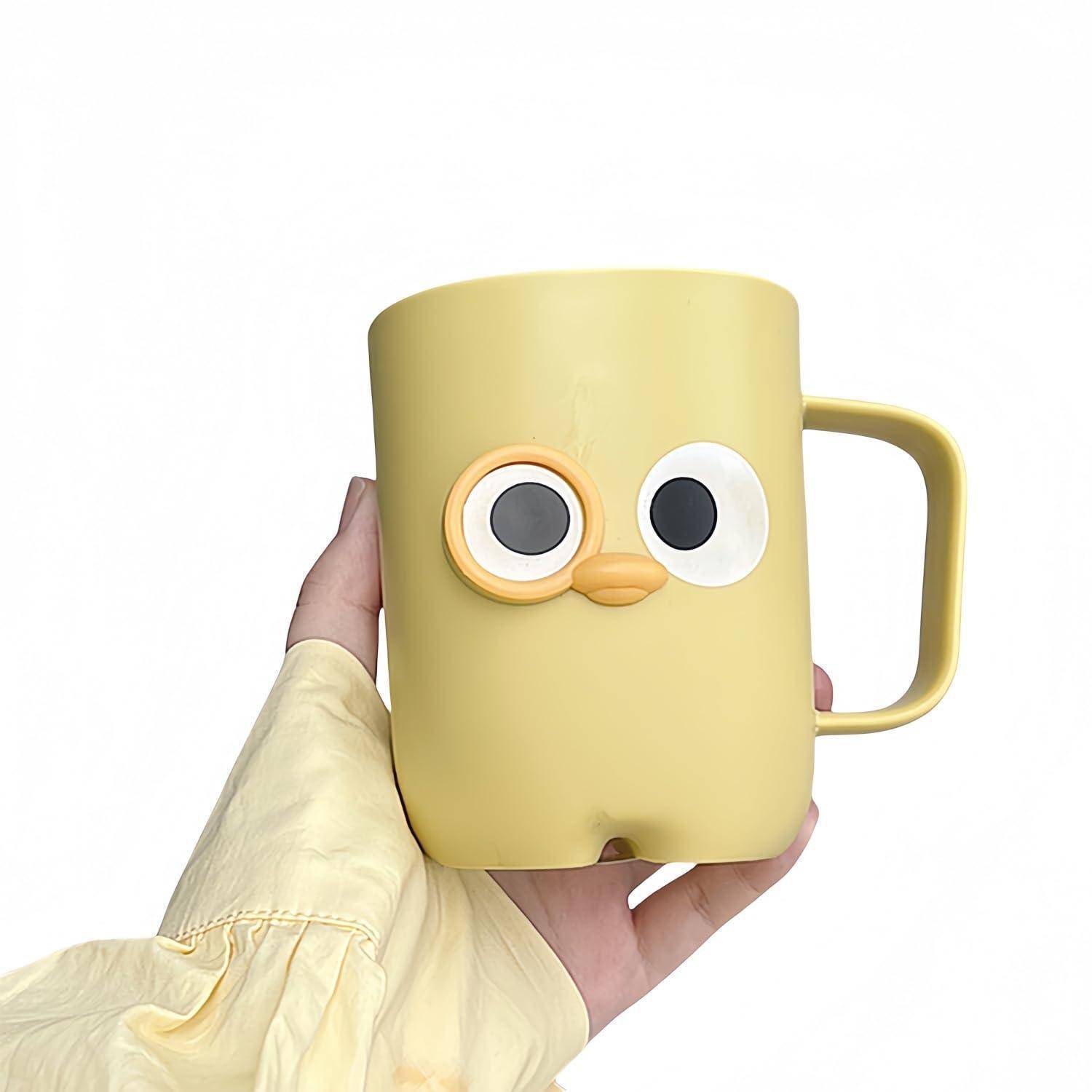 Hand hält eine gelbe Tasse mit einem Cartoon-Gesicht, großen Augen und einer kleinen schnabelartigen Nase auf weißem Hintergrund.