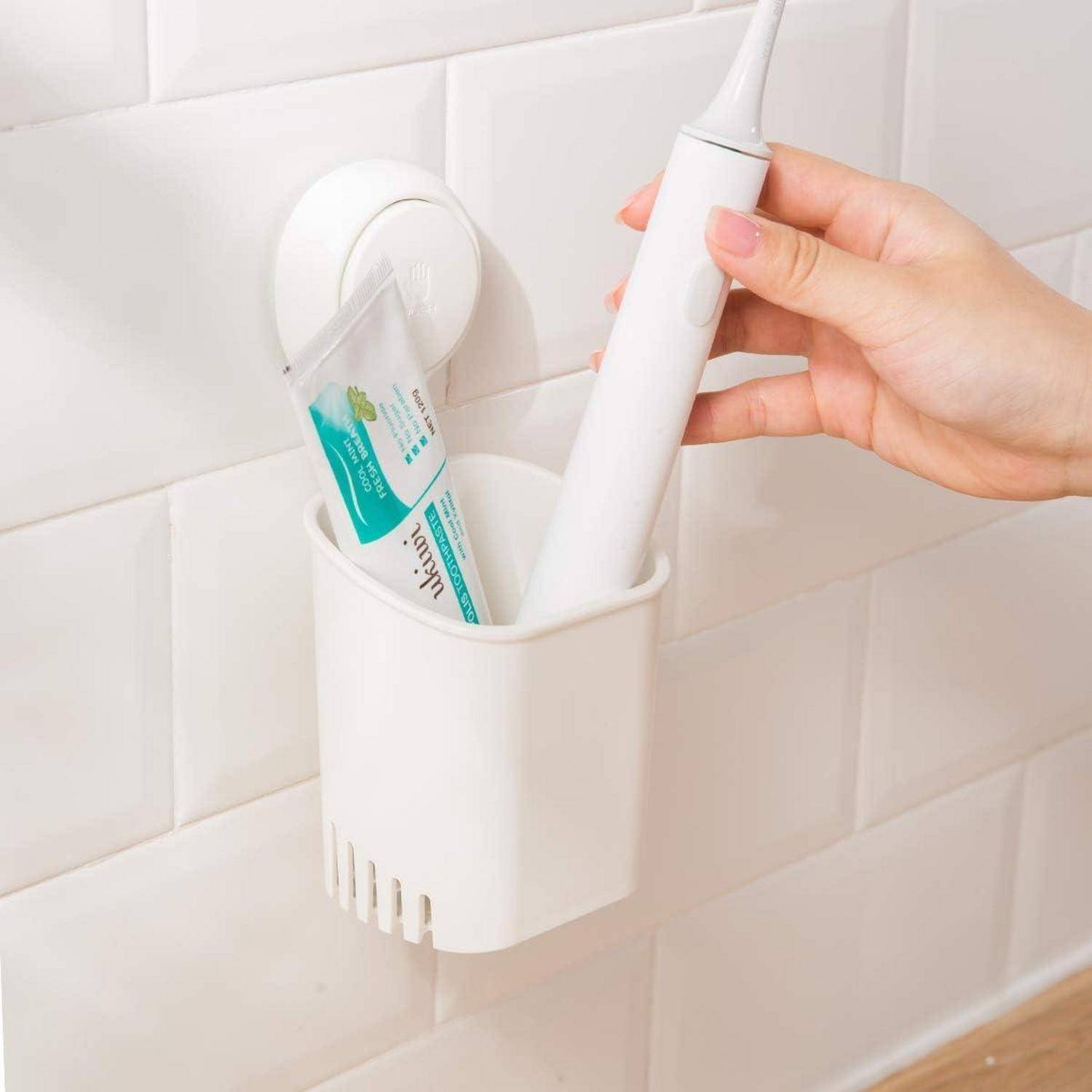 Hand, die eine elektrische Zahnbürste in einen an der Wand angebrachten Halter neben einer Tube Zahnpasta im Badezimmer einsetzt.