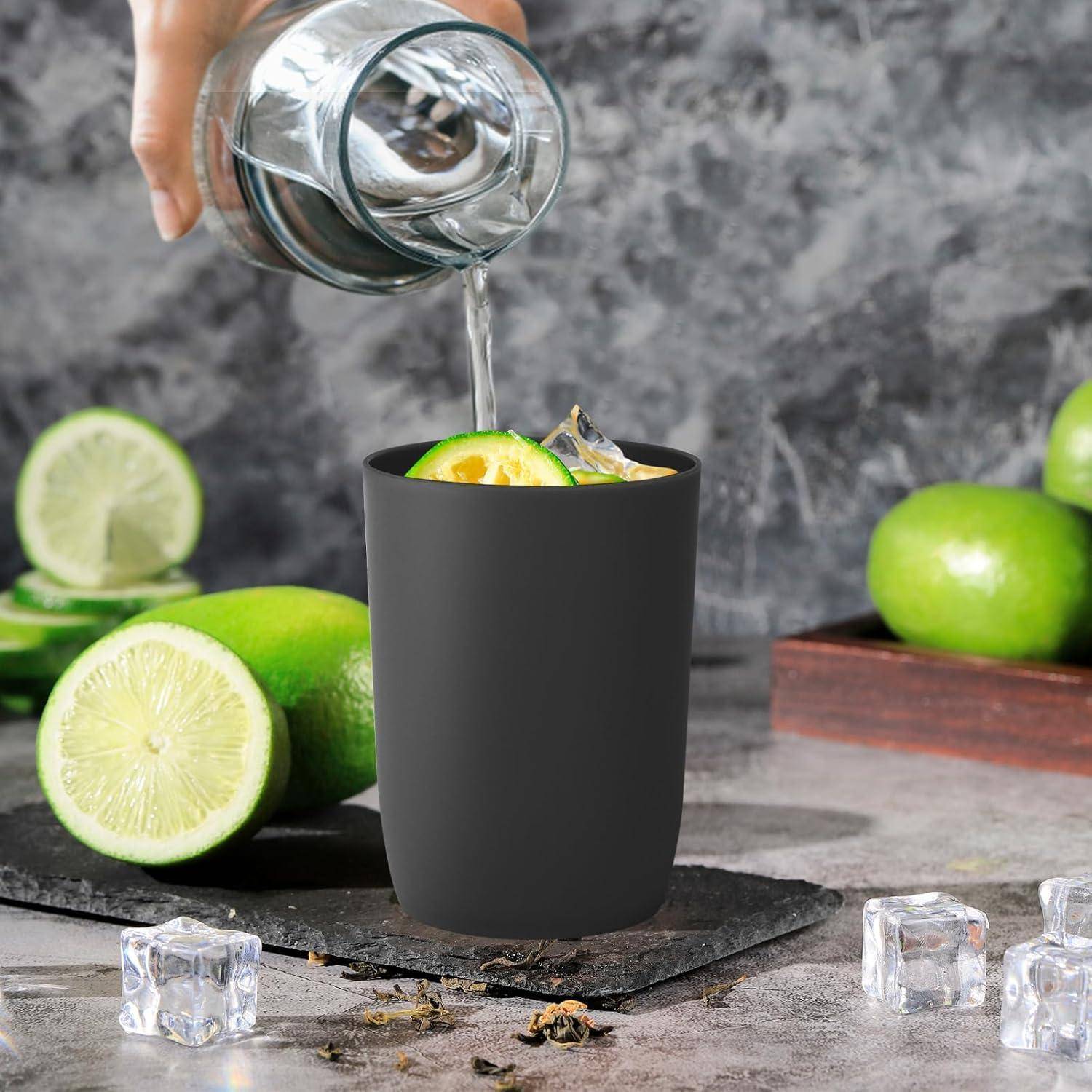 Eine Hand gießt klare Flüssigkeit aus einem Glas in eine schwarze Tasse mit Limettenscheiben und Eis, mit Limetten und Eiswürfeln darum herum.