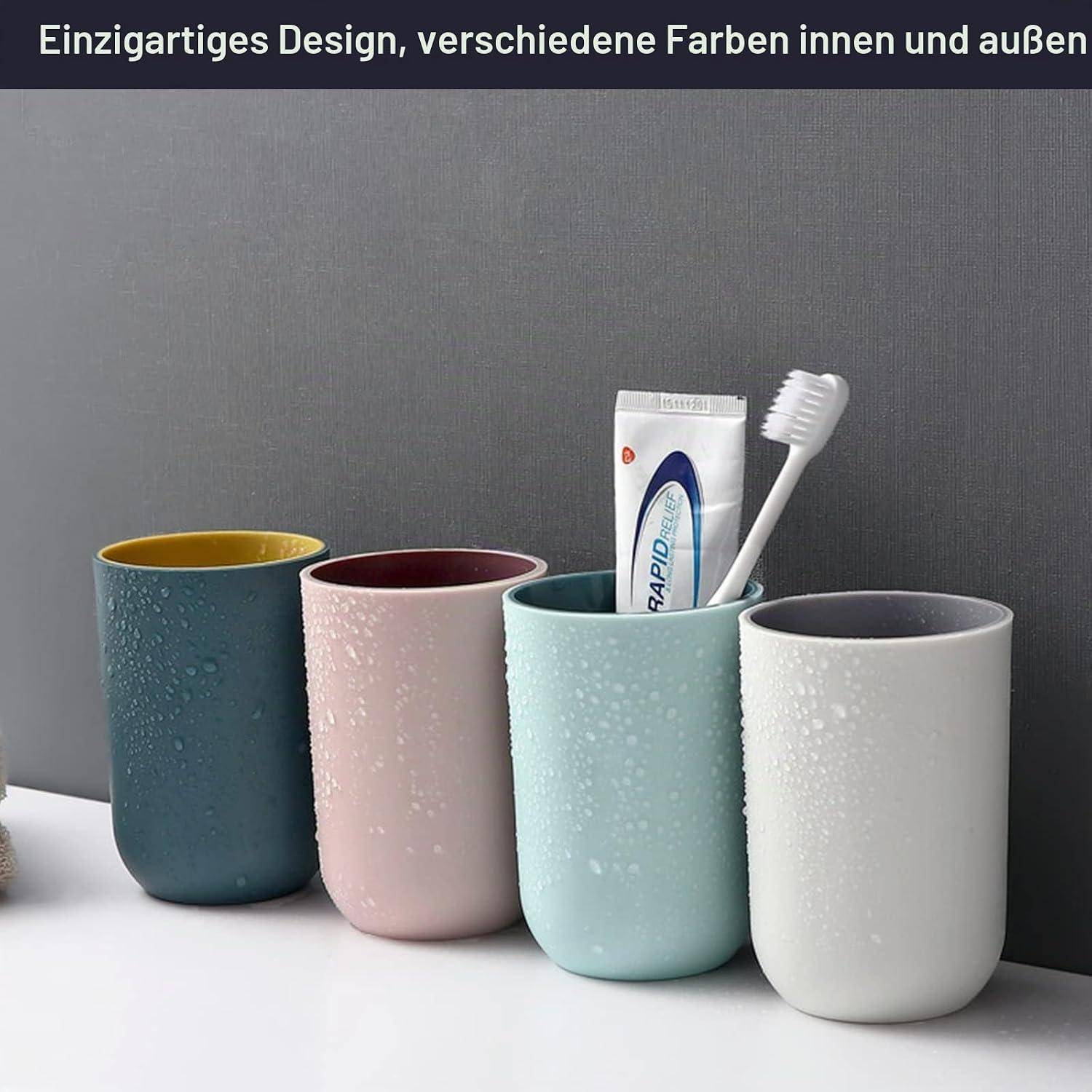 Vier strukturierte Keramik-Zahnbürstenbecher in Blaugrün, Rosa, Minzgrün und Weiß, einer mit einer Zahnbürste und Zahnpasta gefüllt, vor einer grauen Wand.