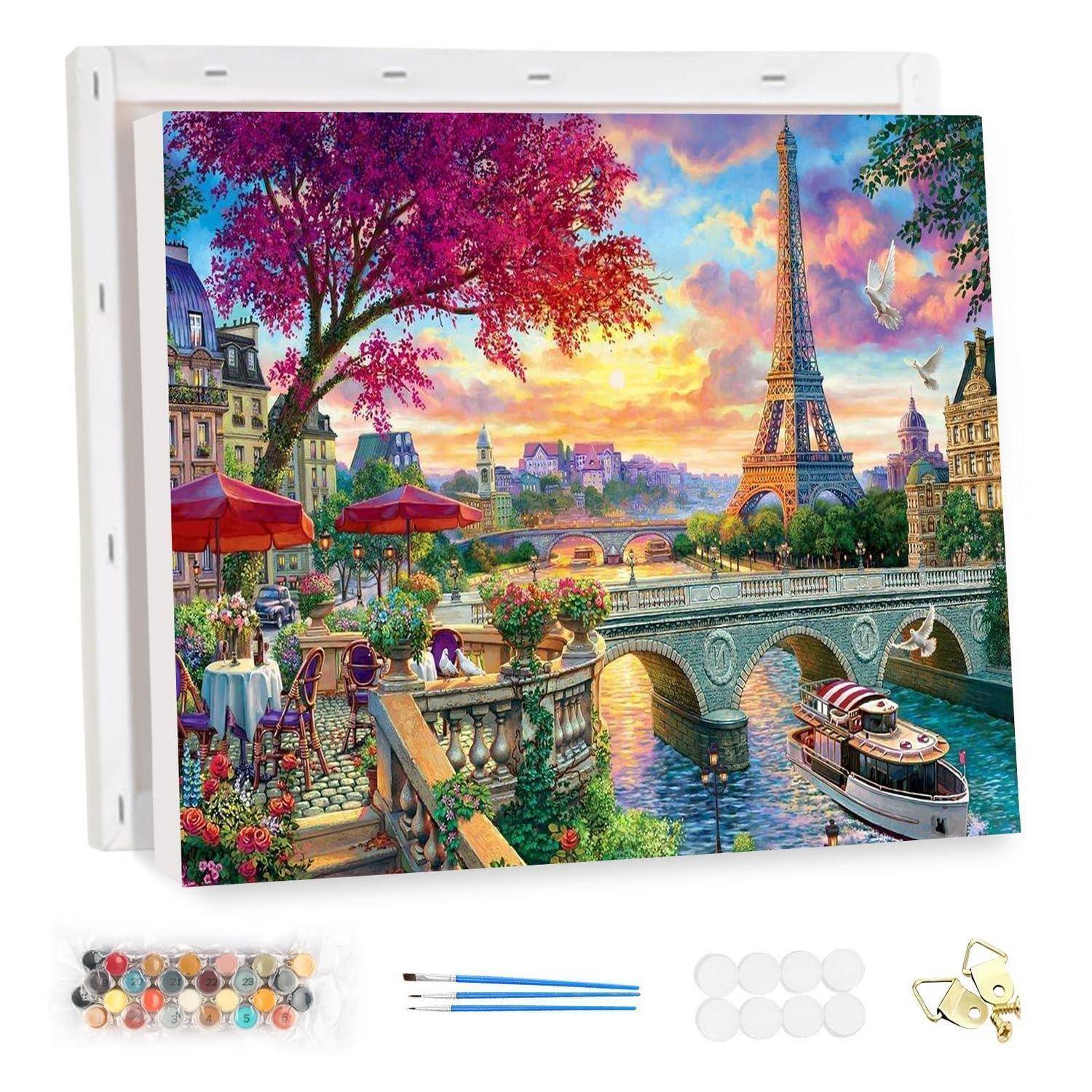 Leinwand-Malset mit einer farbenfrohen Pariser Szene mit dem Eiffelturm, einer Flussbrücke, Cafétischen und einem Boot, plus Malutensilien darunter.