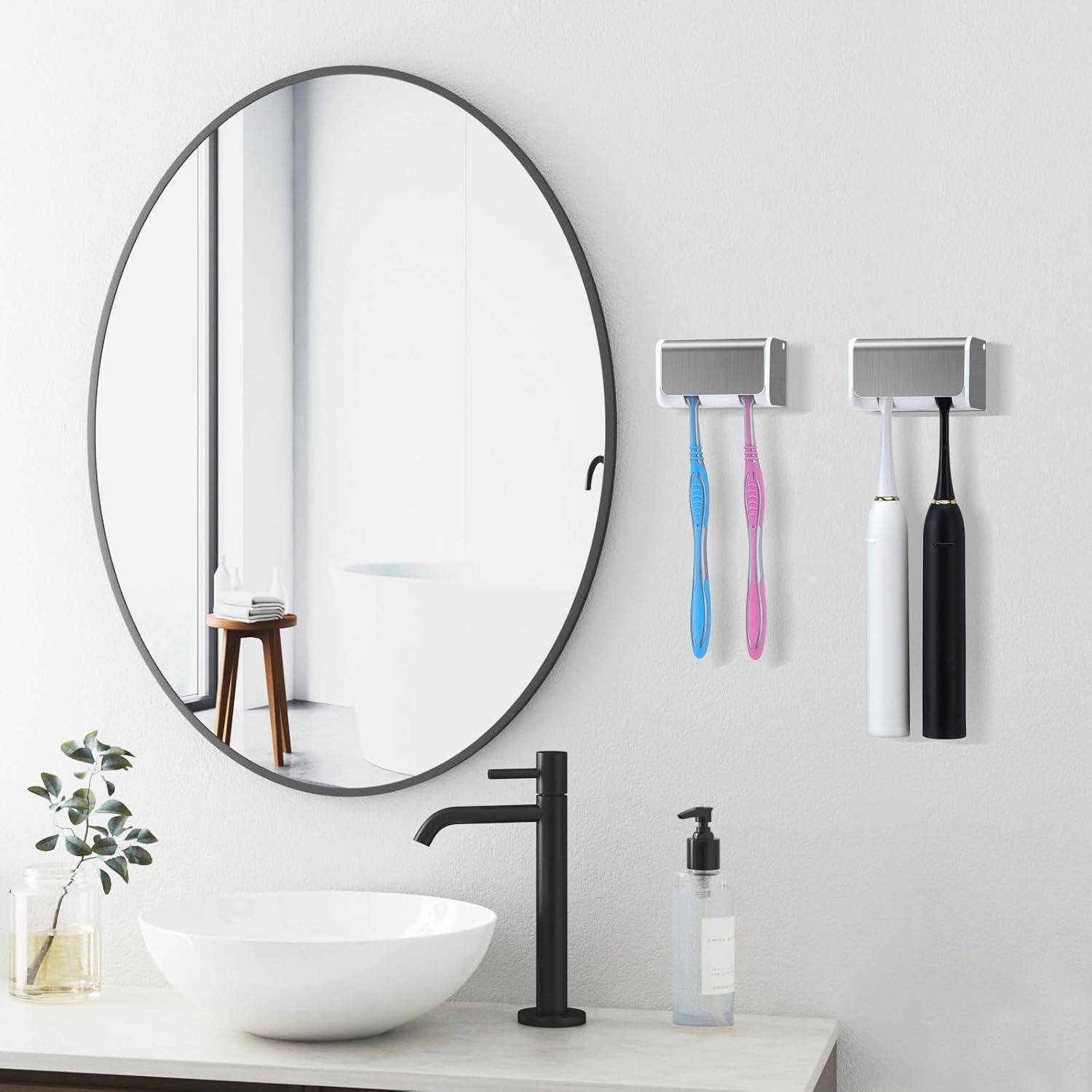 Minimalistische moderne Badezimmerkommode mit ovalem Spiegel, weißem Aufsatzwaschbecken, schwarzem Wasserhahn, Zahnbürstenhaltern, Seifenspender und einer kleinen Pflanze auf einer Arbeitsplatte.