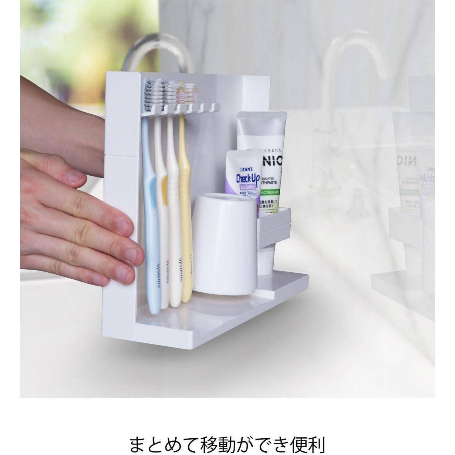 Hand platziert einen wandmontierten Badezimmer-Organizer mit Zahnbürsten, Zahnpasta und einem Becher; japanischer Text lautet „Praktisch, um zusammen mitzunehmen