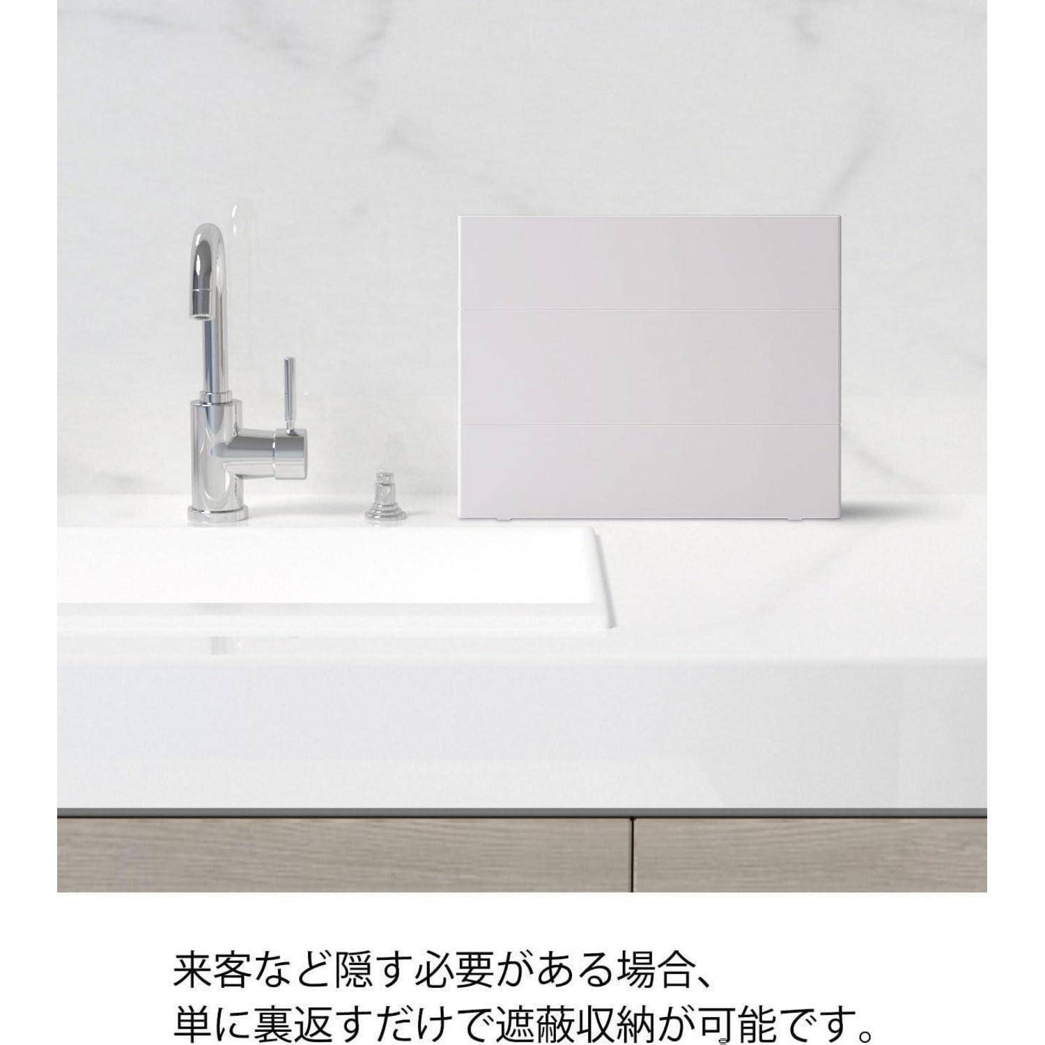 Minimalistische weiße Küchenspüle mit einem Chromhahn, einer kleinen Flasche und einem leeren Panel; japanischer Text darunter besagt, dass es die Küche bei Bedarf verbergen kann.