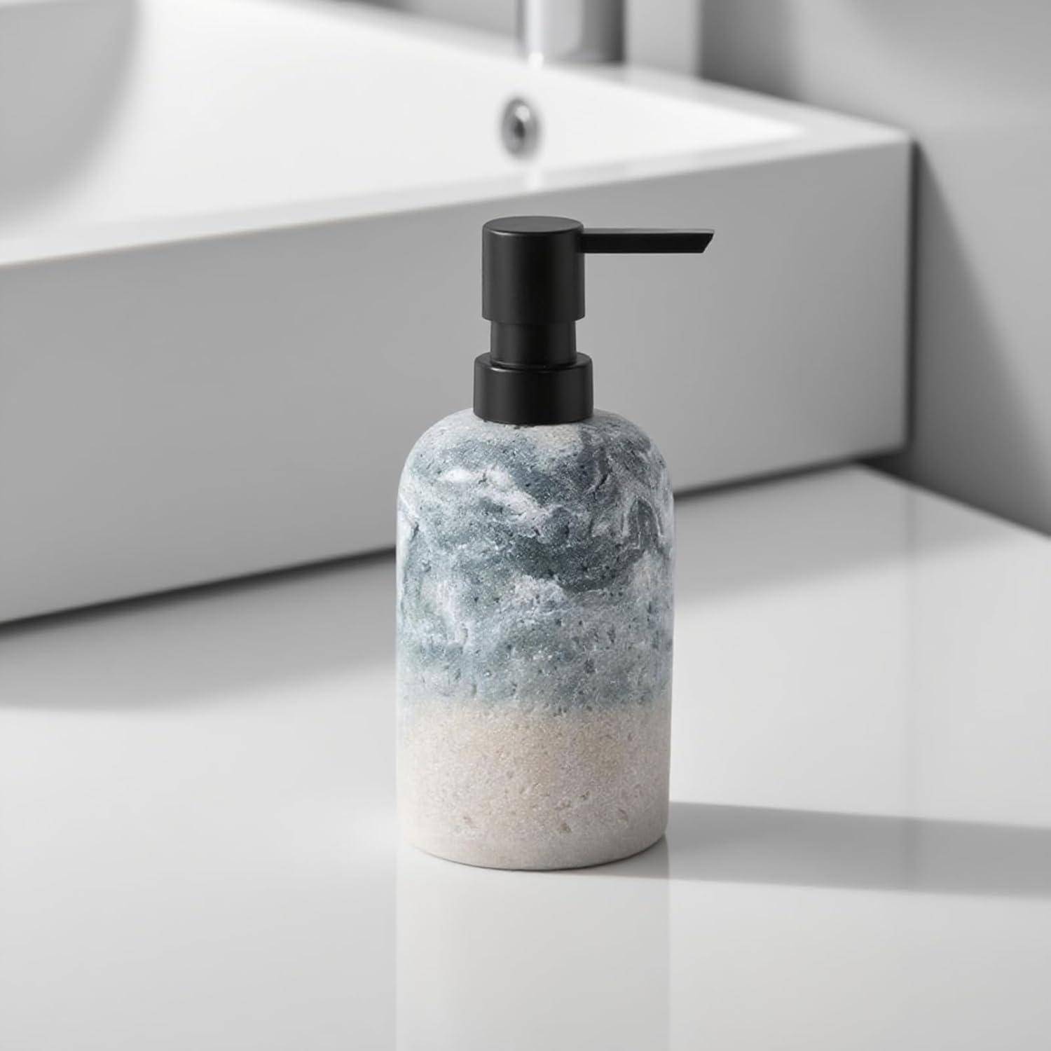 Ein Seifenspender mit einer schwarzen Pumpe und einer marmorierten blaugrauen und weißen Flasche, der auf einer Badezimmerablage neben einem Waschbecken steht.