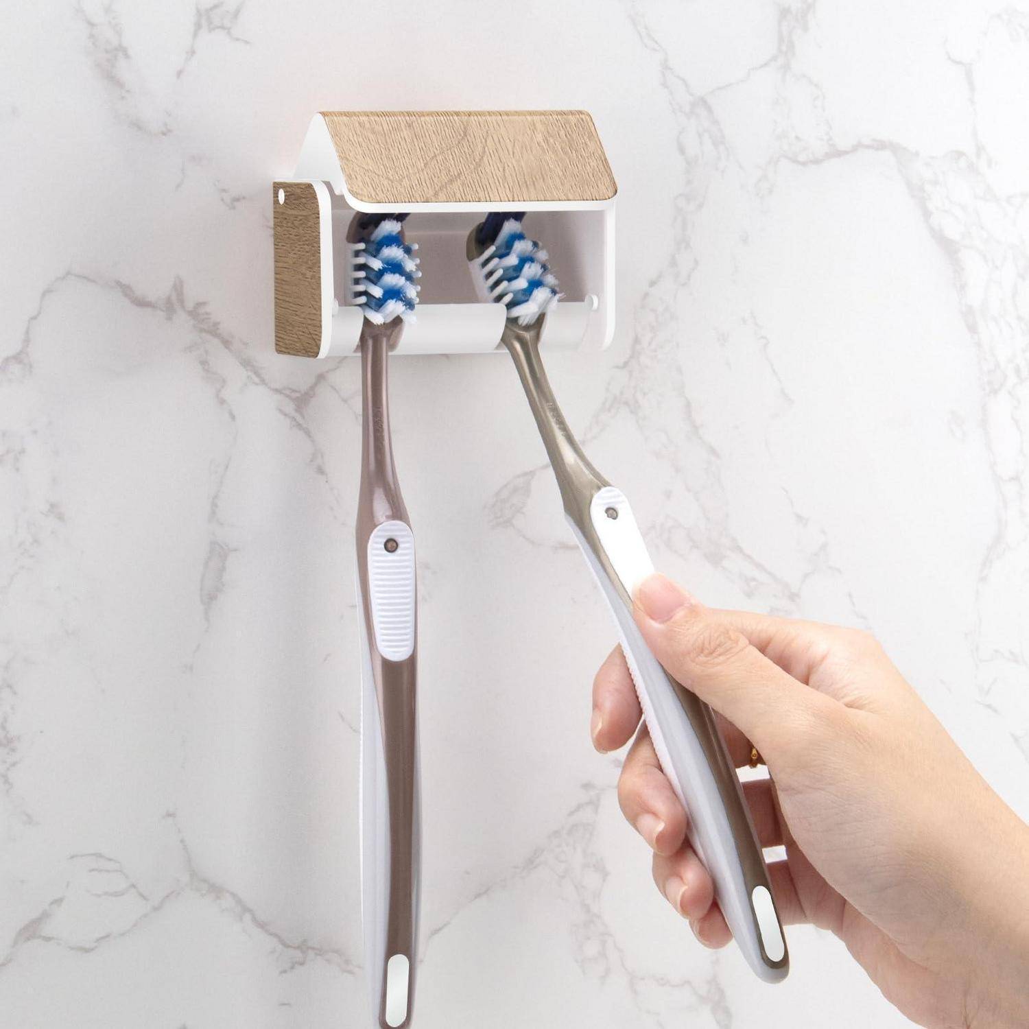 Hand, die eine Zahnbürste in einen an der Wand montierten Halter mit zwei elektrischen Zahnburstköpfen gegen einen Marmormuster-Hintergrund legt.