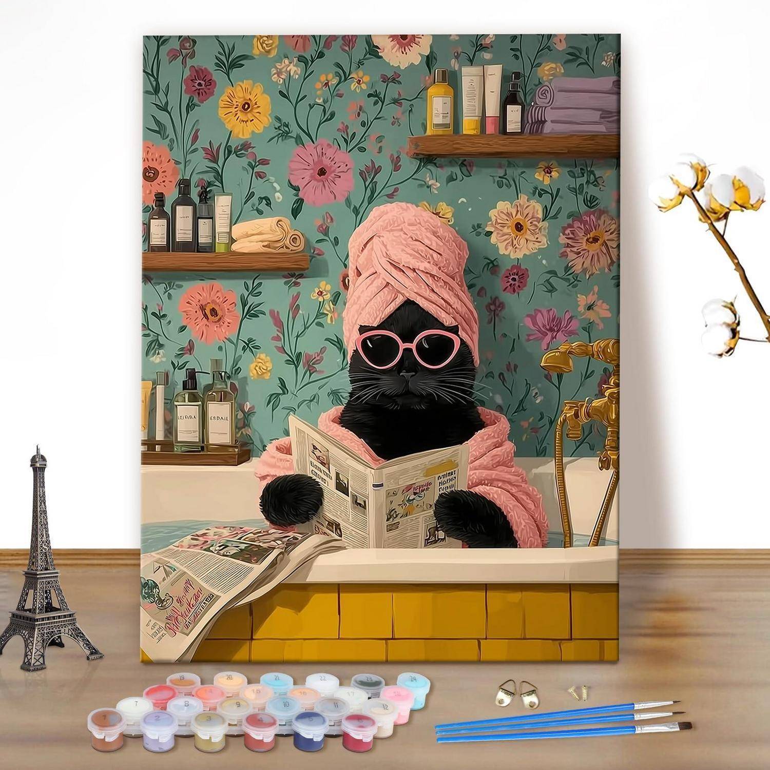 Eine schwarze Katze in einem rosa Handtuch und Sonnenbrille liest eine Zeitung in einer Badewanne, mit Malmaterialien, einem Miniatur-Eiffelturm und floraler Tapete hinter sich.