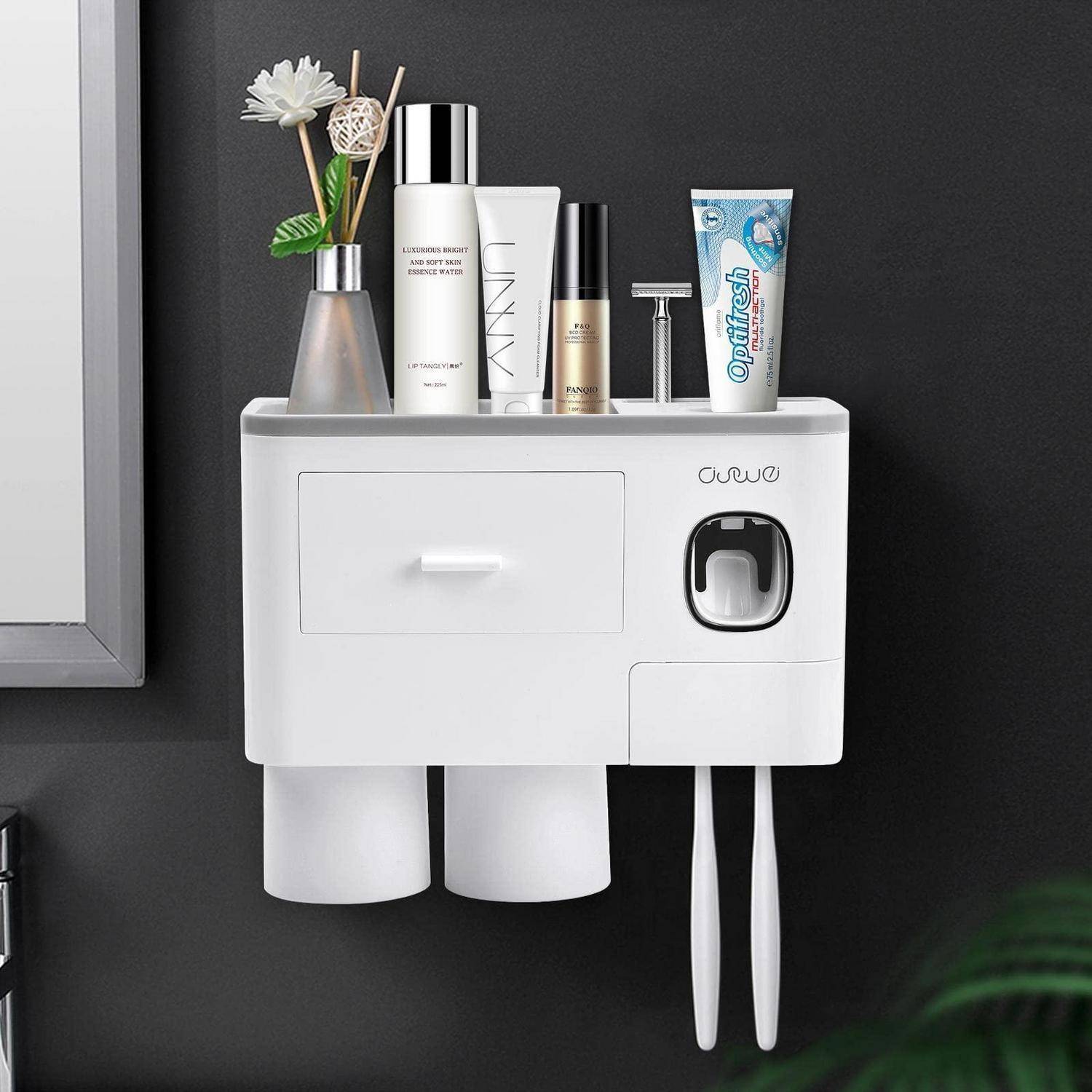 An der Wand montierter weißer Badezimmerorganizer mit Schrank, Zahnbürstenhalter und Toilettenartikeln oben, sowie zwei hängenden Bechern und zwei Zahnbürsten unten.
