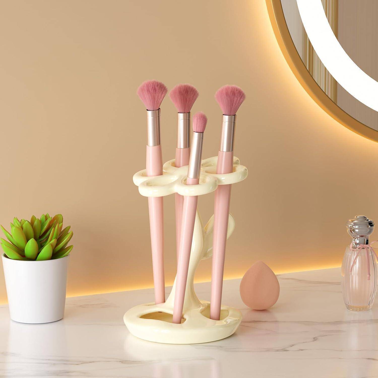 Rosa Makeup-Pinsel-Set in einem cremefarbenen Ständer auf einer Marmor-Frisiertischplatte, mit einem kleinen Sukkulenten, Schwamm und Parfümflasche in der Nähe.
