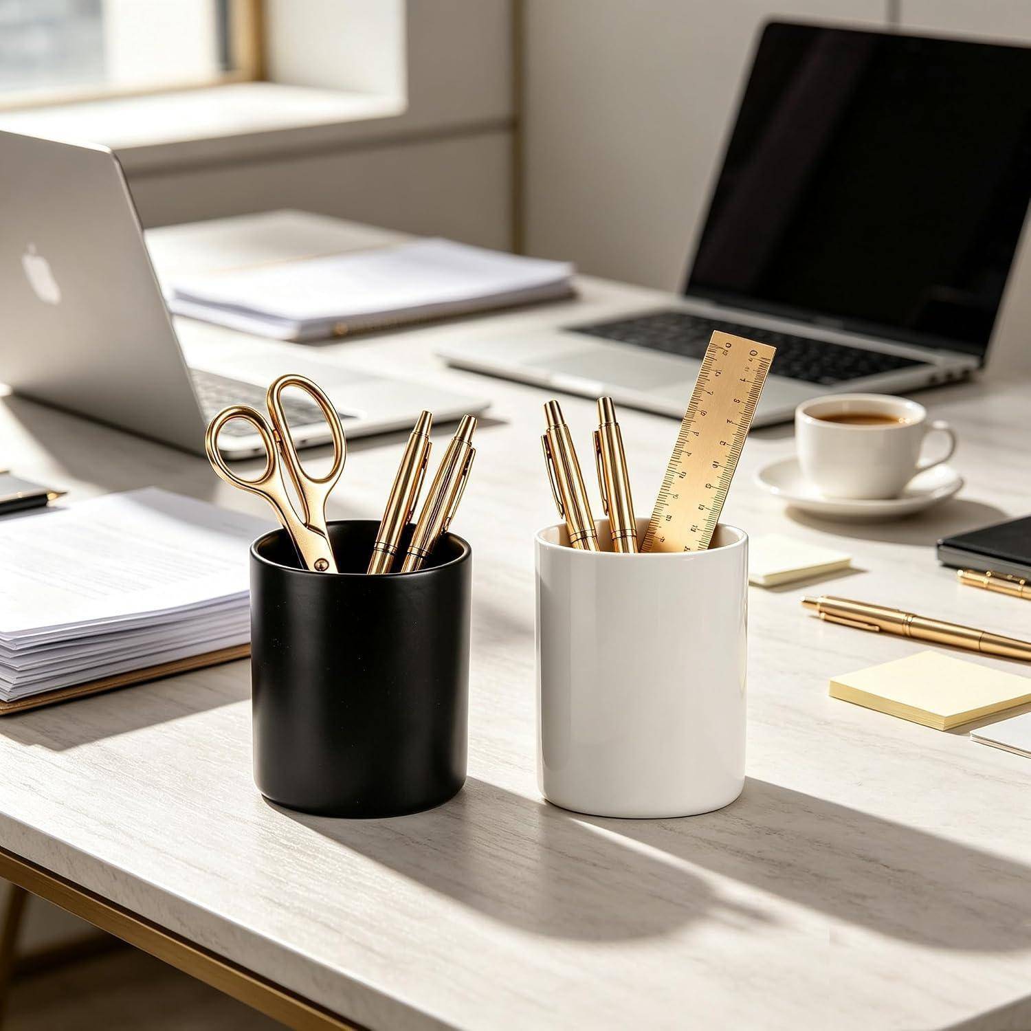 Bürotisch mit zwei Stiftbechern, die Scheren, Stifte und ein Lineal enthalten, daneben Laptops, Papiere und eine Kaffeetasse.