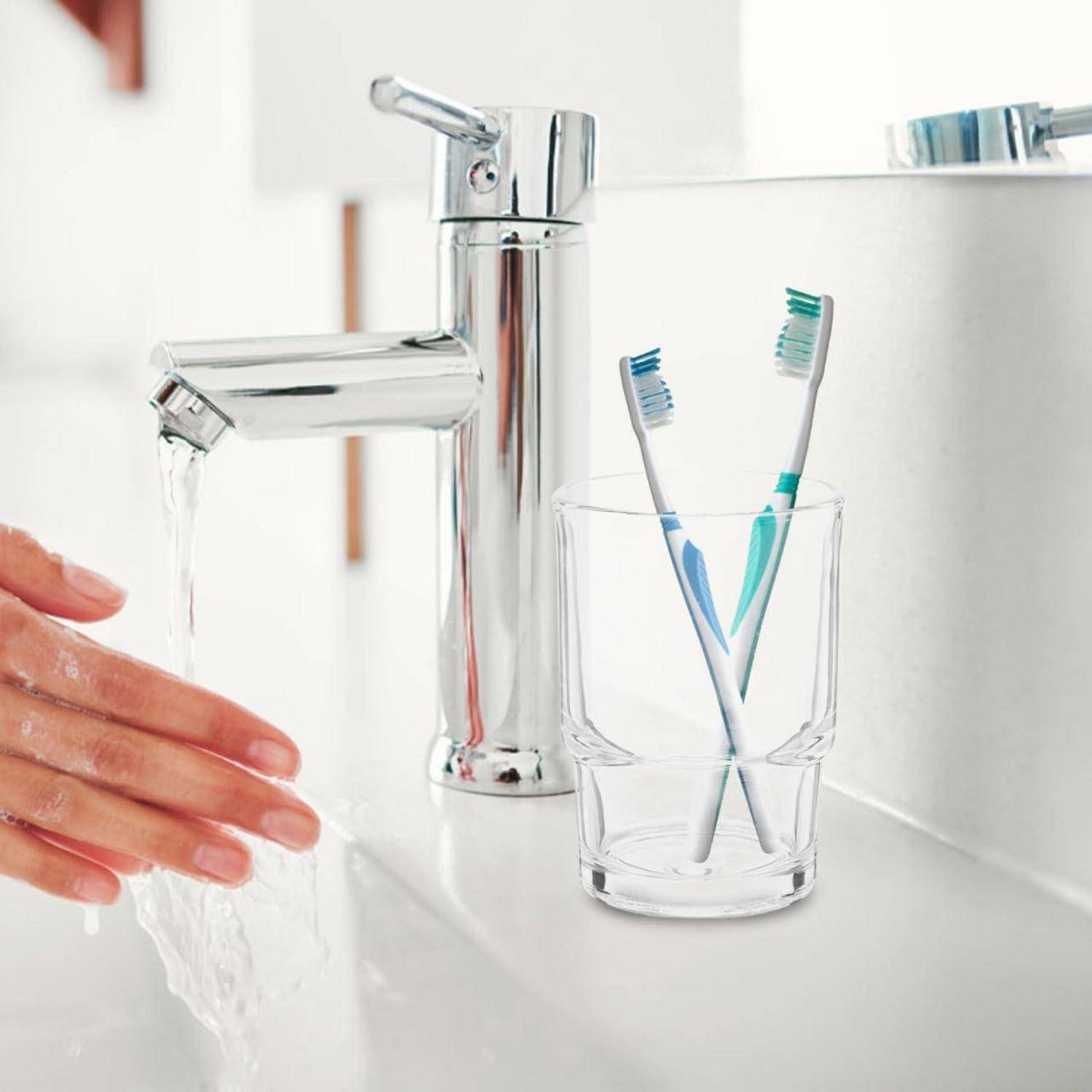 Händewaschen unter einem fließenden Badezimmerwasserhahn neben zwei Zahnbürsten in einem Glas.