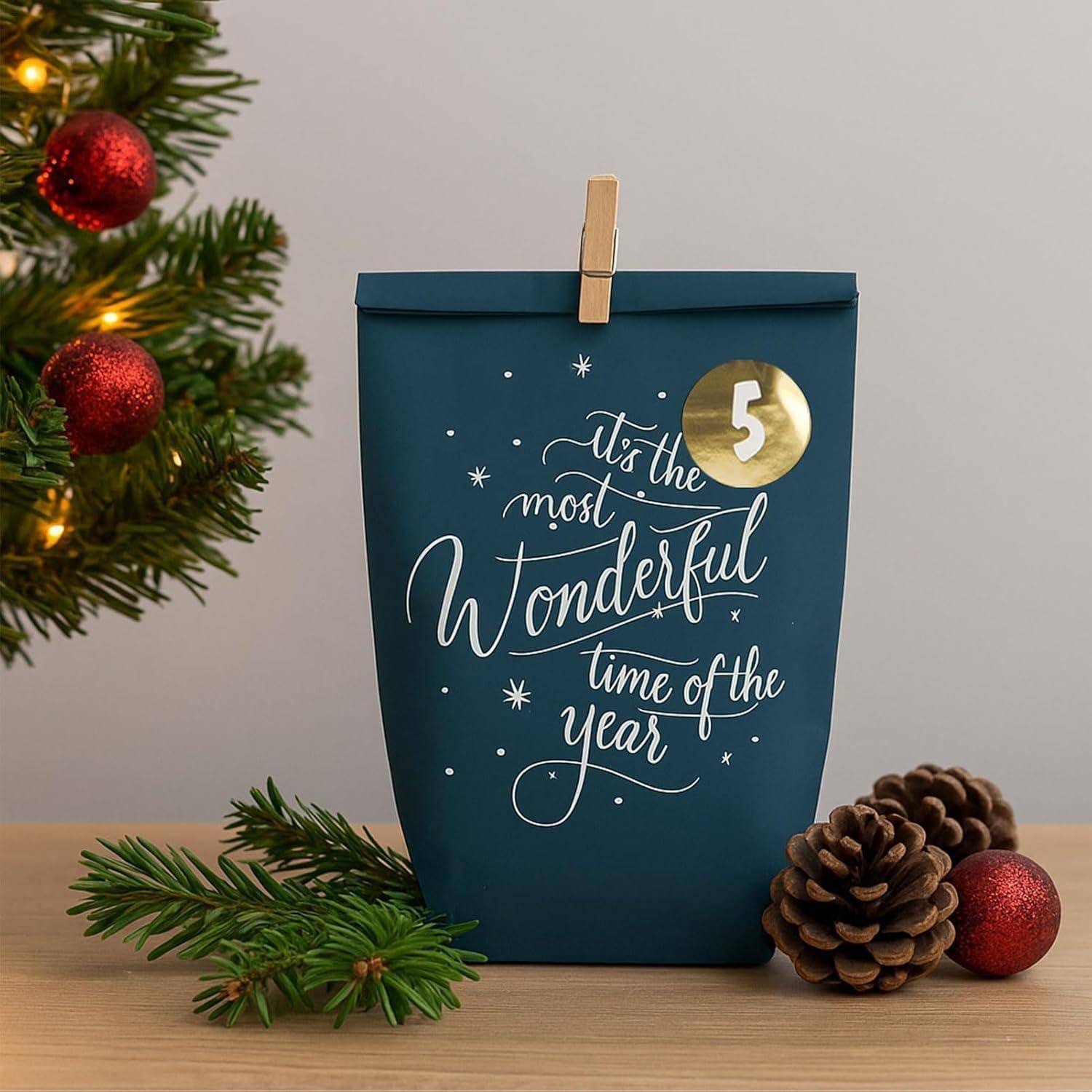 Blaue Weihnachtsgeschenktüte auf einem Tisch mit Clip und Kieferndekor, bedruckt mit „'Tis the most Wonderful time of the Year