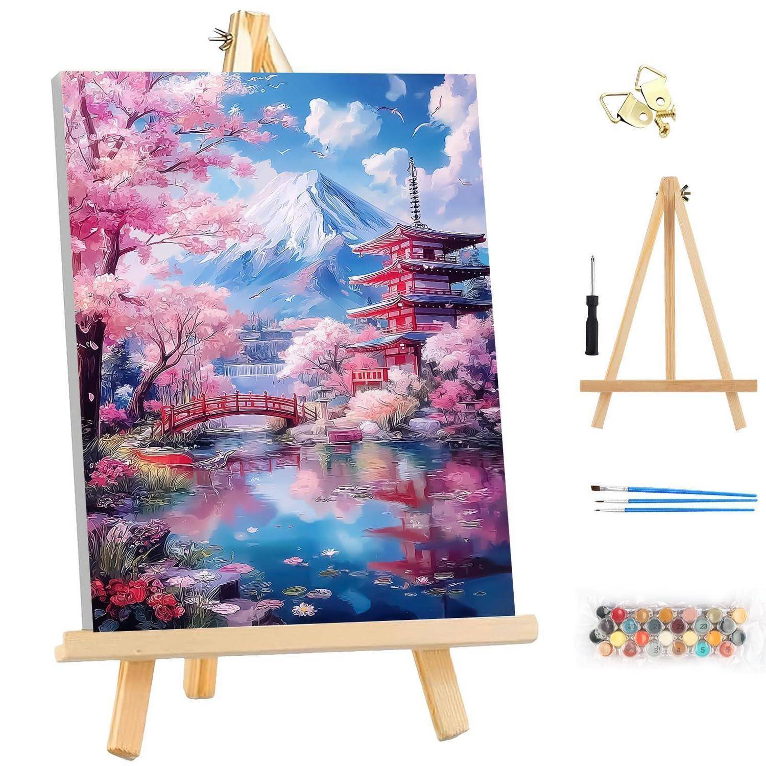 Ein Malset zeigt eine Kirschblüten-Landschaft auf einer Staffelei, mit einem Berg, einer Pagode, einer Brücke und einem Teich, sowie Pinseln und Zubehör.