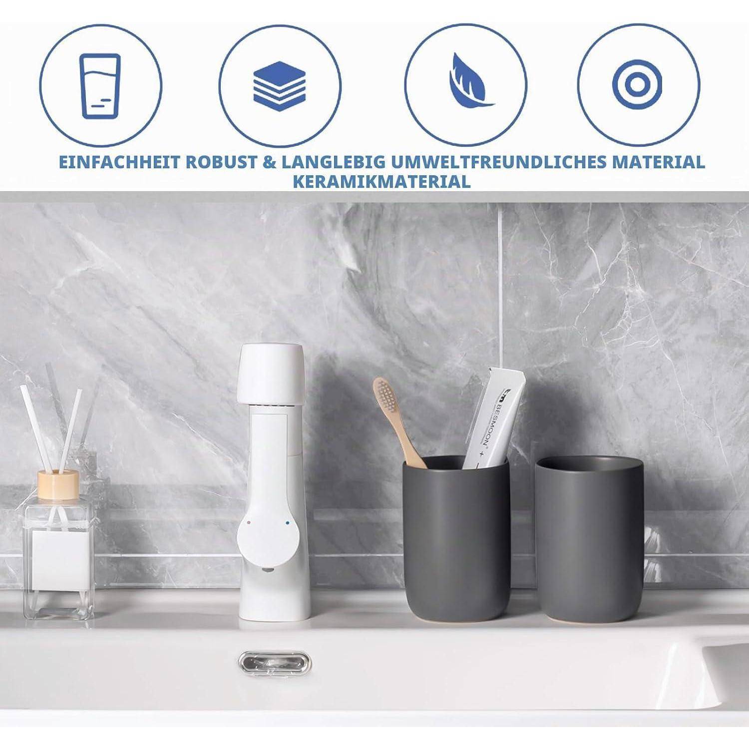 Minimalistische Badezimmerwaschtisch mit weißem Spender, Zahnbürste und zwei dunklen Tassen vor Marmor-Optik-Wand; deutscher Text besagt, dass das Keramikmaterial einfach, robust, langlebig und umweltfreundlich ist.