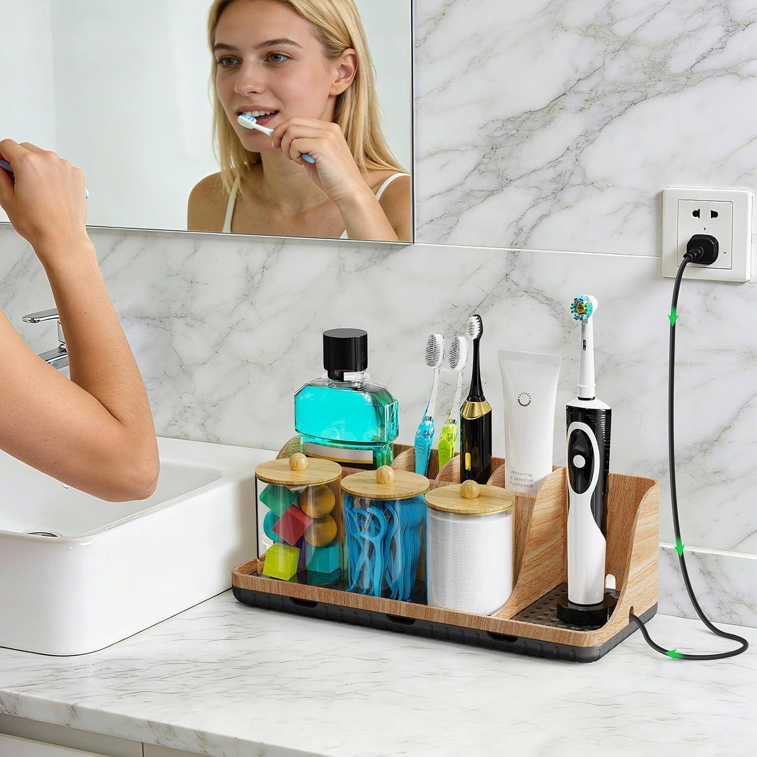 Badezimmer-Waschtisch mit einer Frau, die sich die Zähne im Spiegel putzt, und einem Arbeitsplatz-Organizer, der Zahnbürsten, Zahnpasta, Rasierer und Toilettenartikel neben einem Ladegerät für elektrische Zahnbürsten hält.