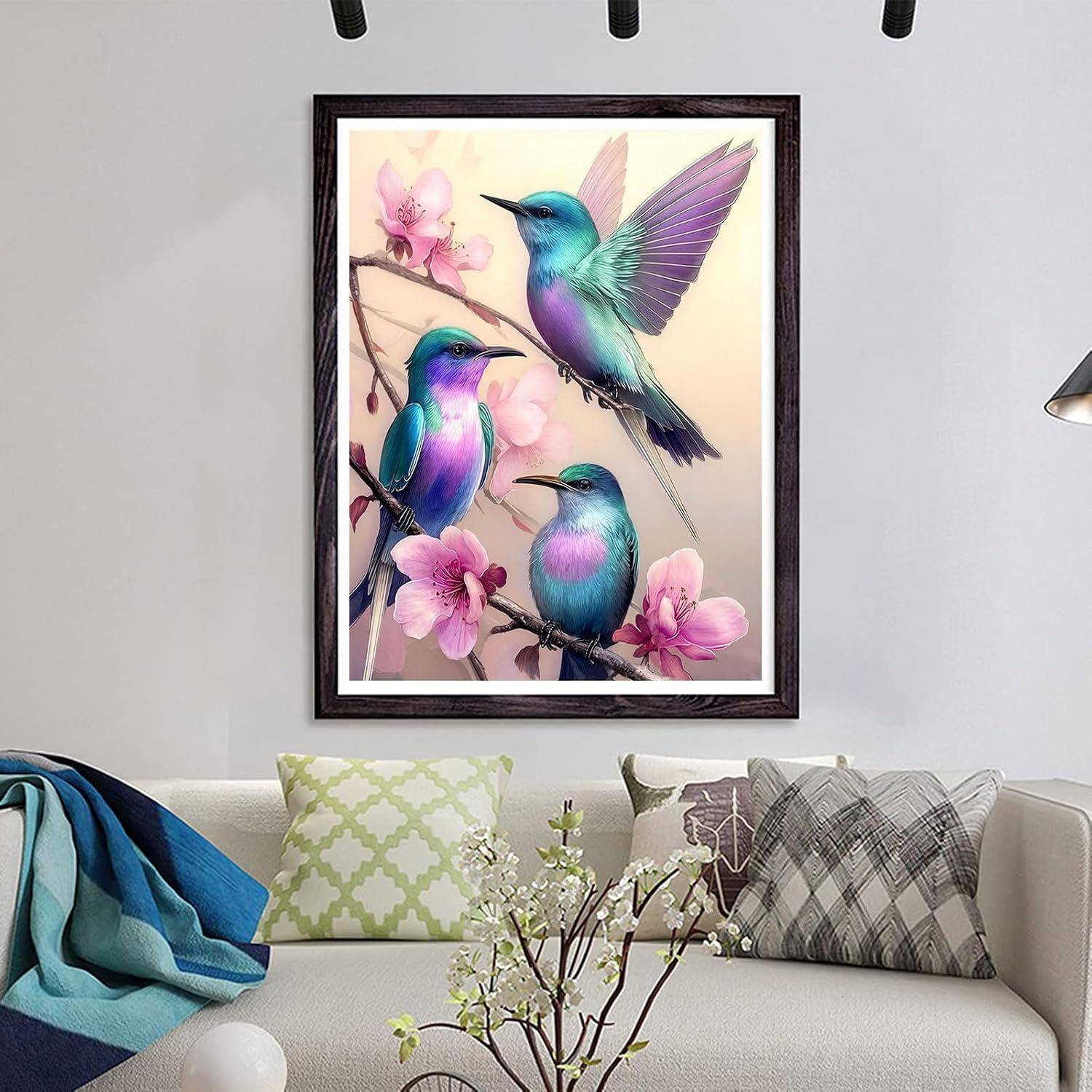 Gerahmte Wandkunst mit drei bunten Kolibris zwischen rosa Blüten über einem Sofa in einem modernen Wohnzimmer.
