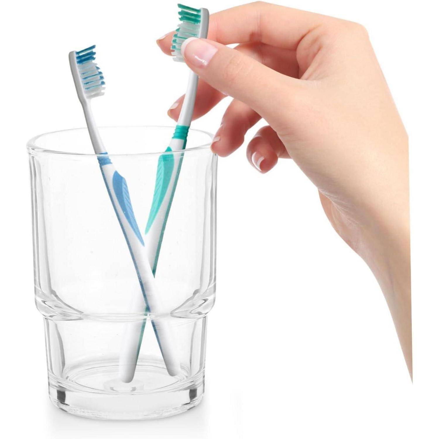 Hand, die eine Zahnbürste in ein Glas mit zwei Zahnbürsten legt.