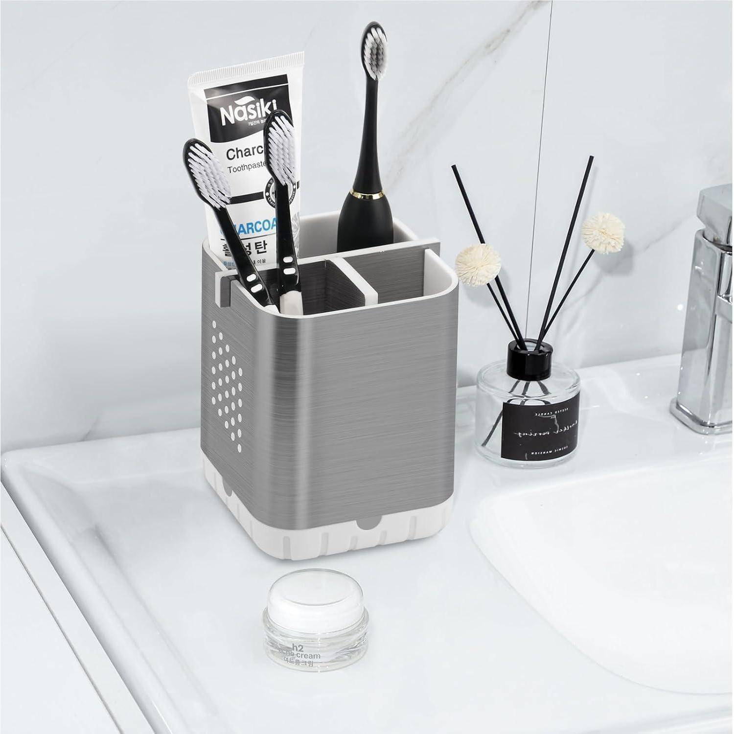 Badezimmer-Waschbecken-Caddy mit Zahnbürsten, Zahnpasta und einer schwarzen Zahnbürste neben einem Raumdiffusor auf einer weißen Arbeitsplatte.