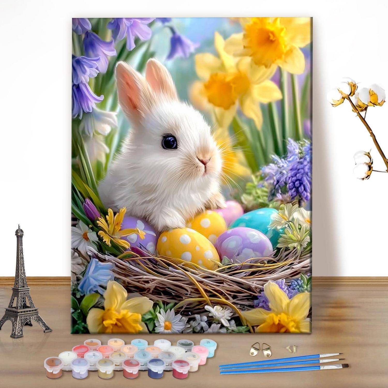 Buntes Oster-Gemälde eines weißen Kaninchens in einem Nest mit bemalten Eiern und Blumen, ausgestellt in einem Studio mit Kunstbedarf und Mini-Deko.