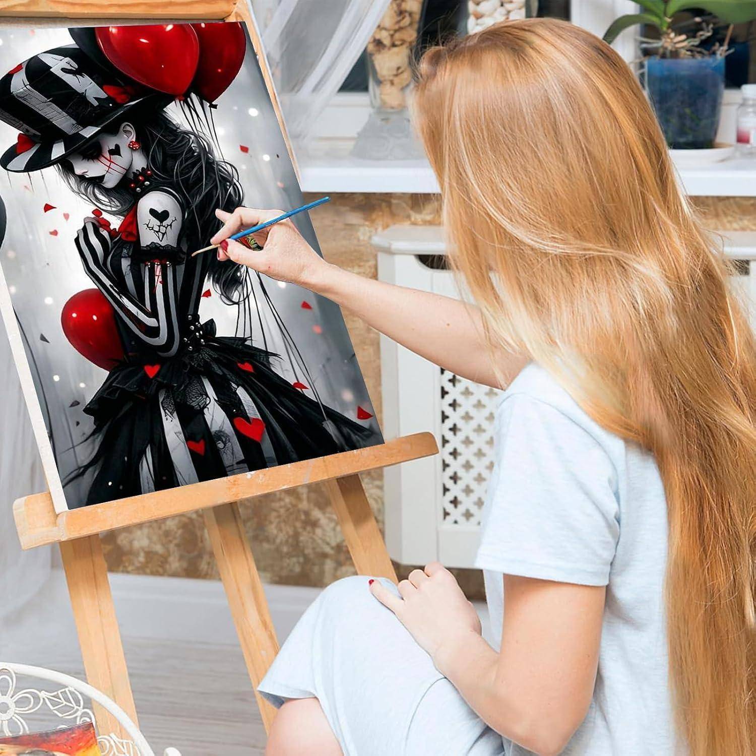 Eine Frau mit langem blondem Haar malt ein schwarz-rotes stilisiertes Porträt auf einer Staffelei in einem hellen Studio.