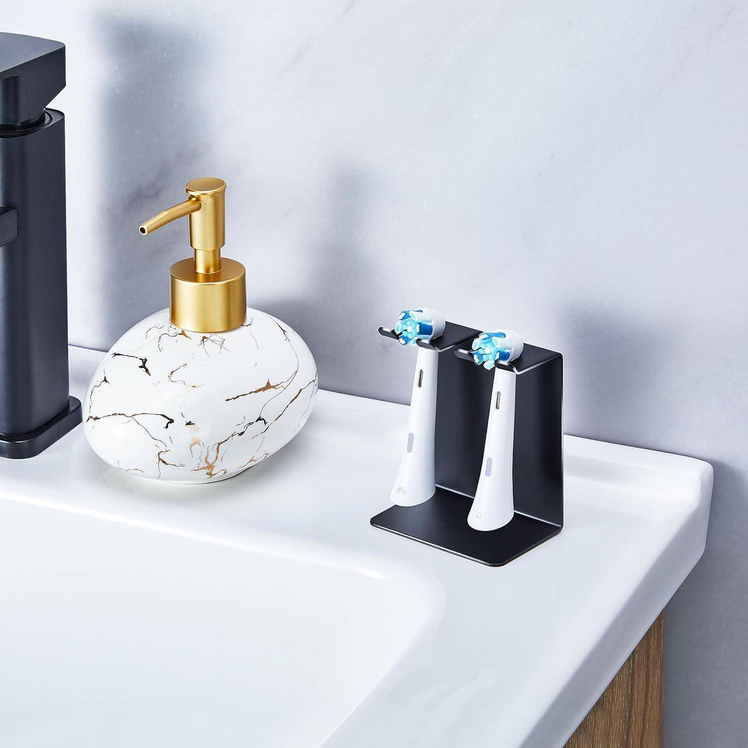 Badezimmer-Waschtischablage mit marmorgemustertem Seifenspender und schwarzem Ständer, der zwei elektrische Zahnbürsten hält, neben einem Wasserhahn.