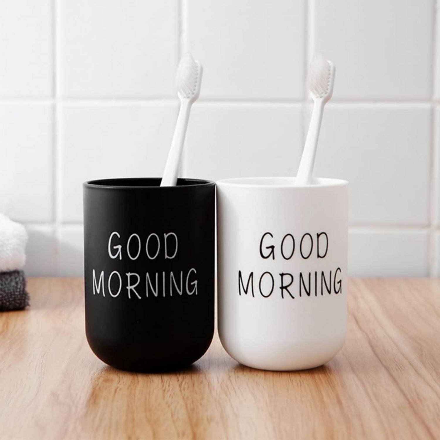 Zwei Zahnbürsten in schwarzen und weißen Bechern mit der Aufschrift „GOOD MORNING