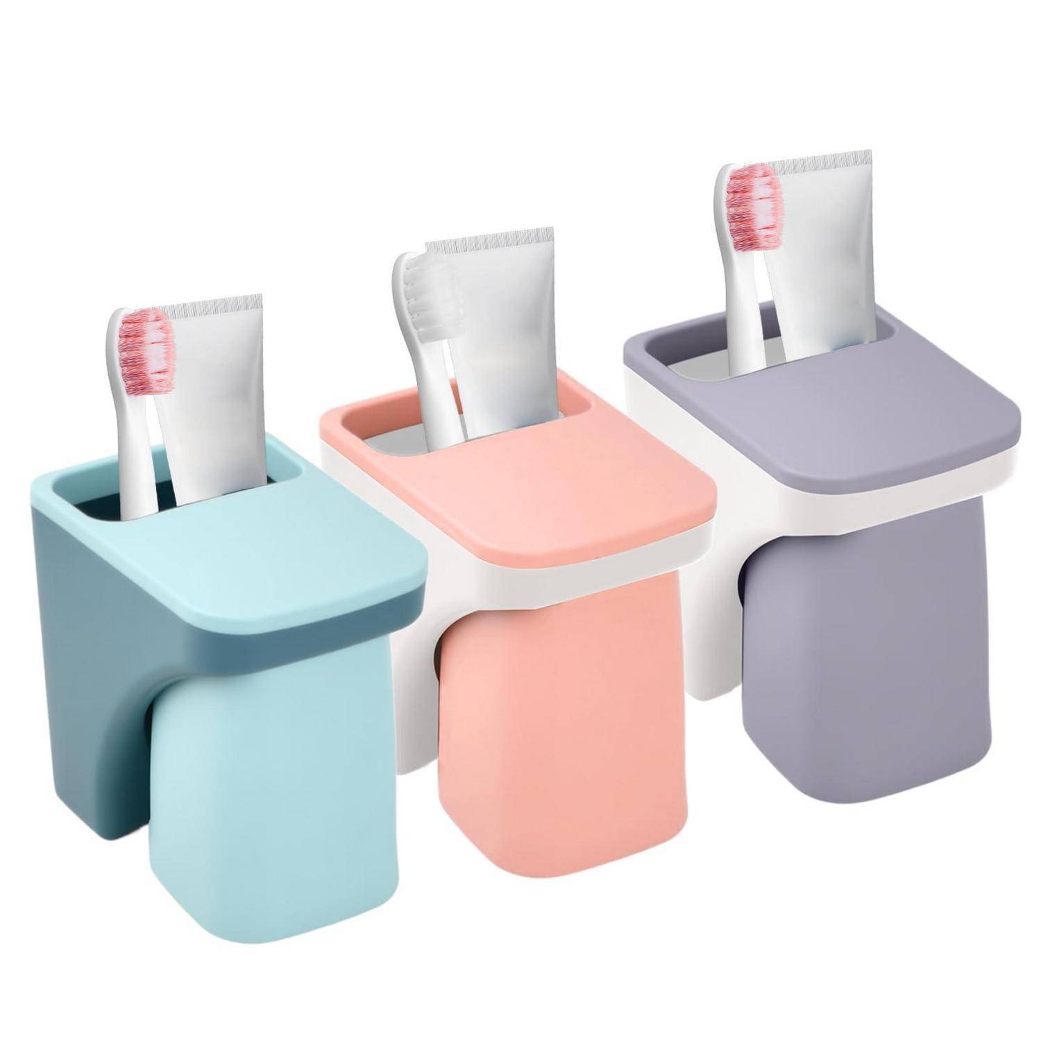 Drei wandmontierte Zahnbürstenhalter in Blau, Rosa und Grau, von denen jeder eine Zahnbürste und eine Zahnpastatube enthält.