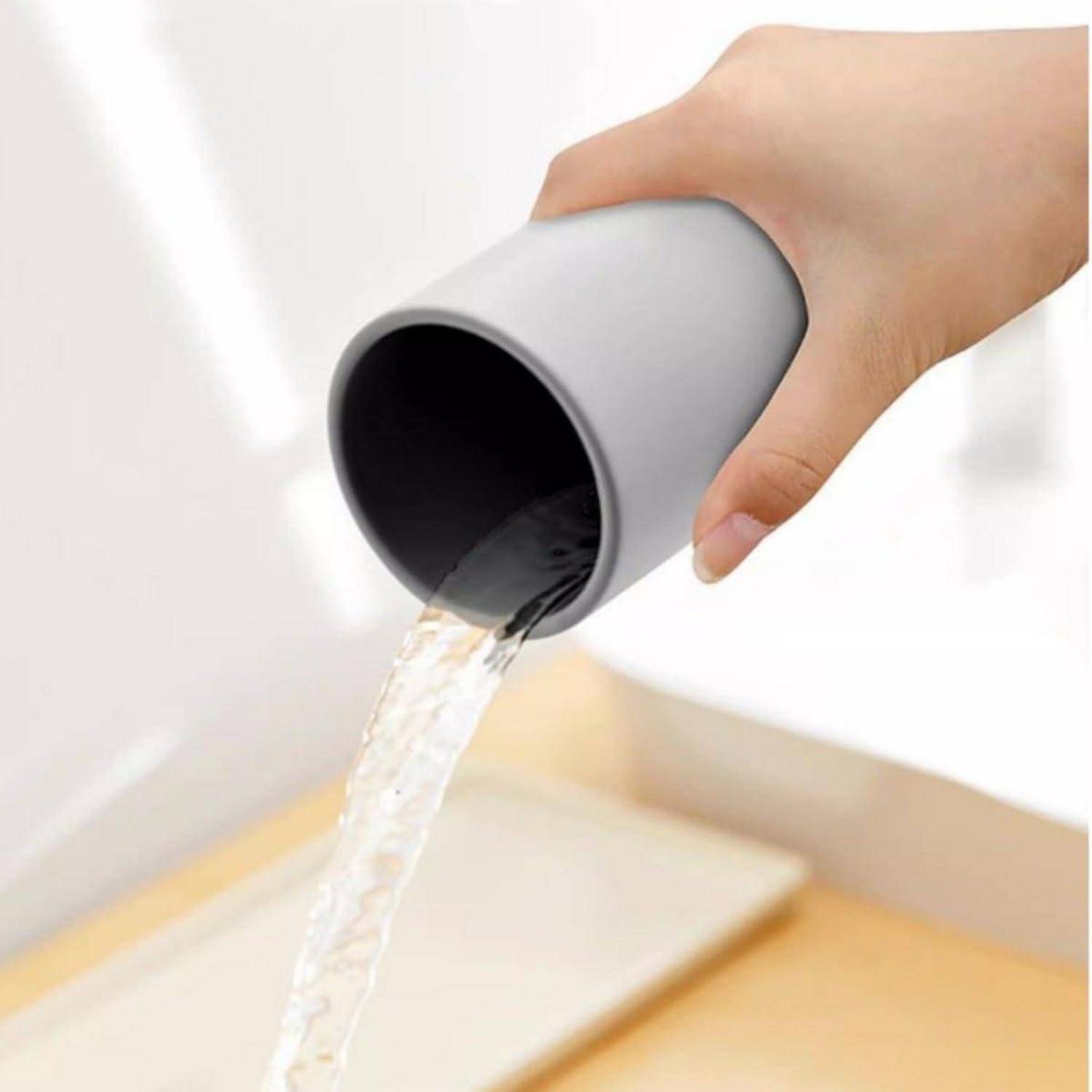 Eine Hand neigt eine graue Tasse und gießt Wasser in ein Waschbecken oder Becken.