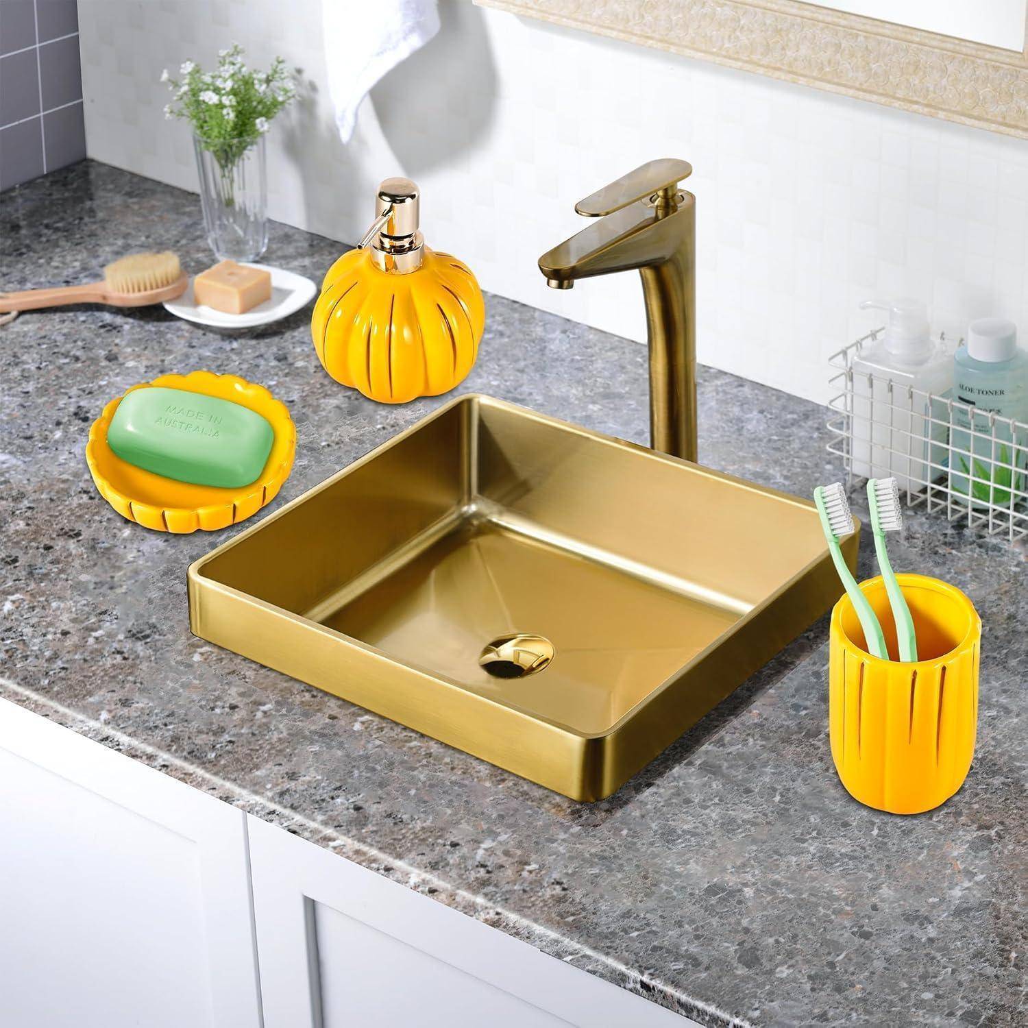 Quadratisches goldenes Badezimmerbecken und Wasserhahn auf grauer Arbeitsplatte mit passendem orange-gelbem Seifenspender, Schüssel und Zahnbürstenbecher; dekoratives Badezimmerset.