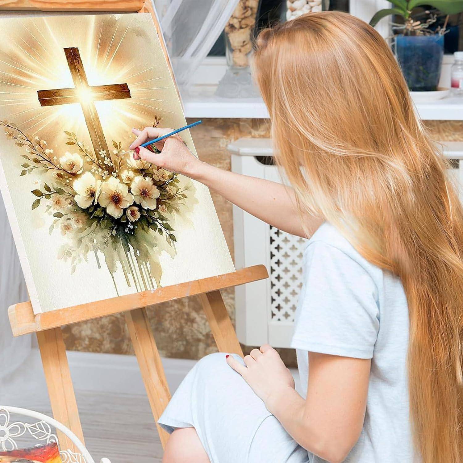 Junge Frau malt ein leuchtendes Kreuz mit Blumen auf einer Staffelei in einem hellen Studio.