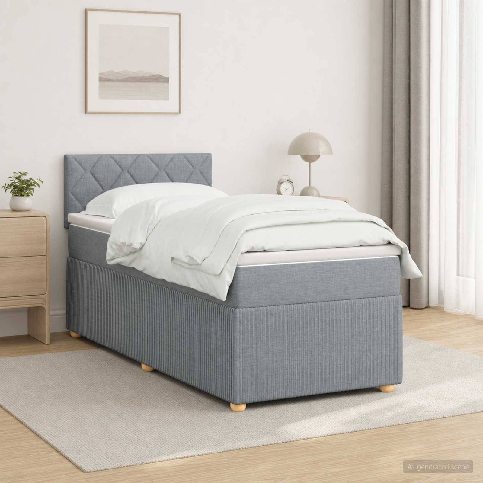 Grau gepolstertes Einzelbett mit weißer Bettwäsche in einem hellen minimalistischen Schlafzimmer, neben einem Nachttisch und einer Lampe in der Nähe eines Fensters.