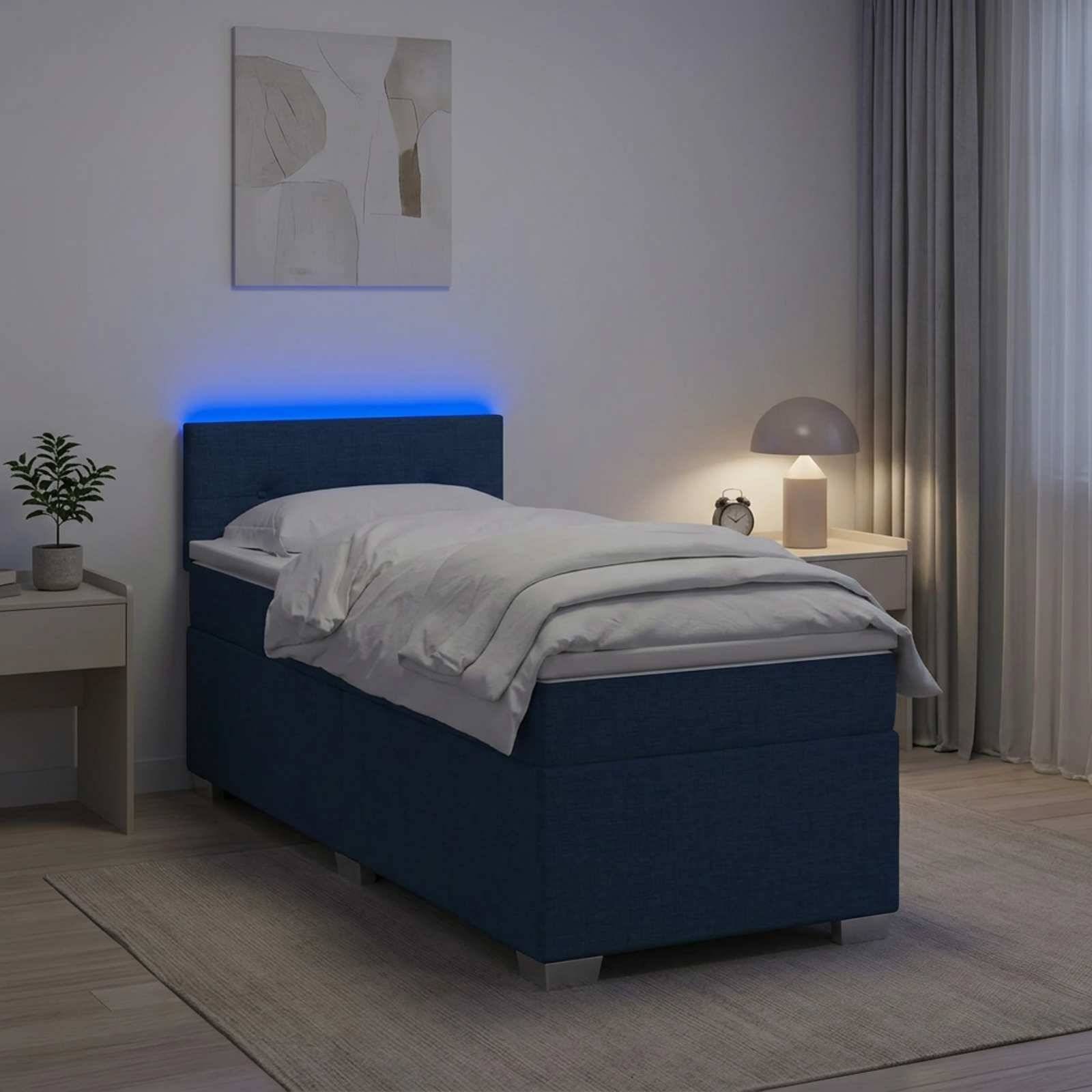 Modernes Schlafzimmer mit einem einzelnen marineblauen Bett, weißer Bettwäsche, blauer Kopfleuchte, Nachttischlampe, Pflanze und Vorhängen in einem minimalistischen Zimmer.