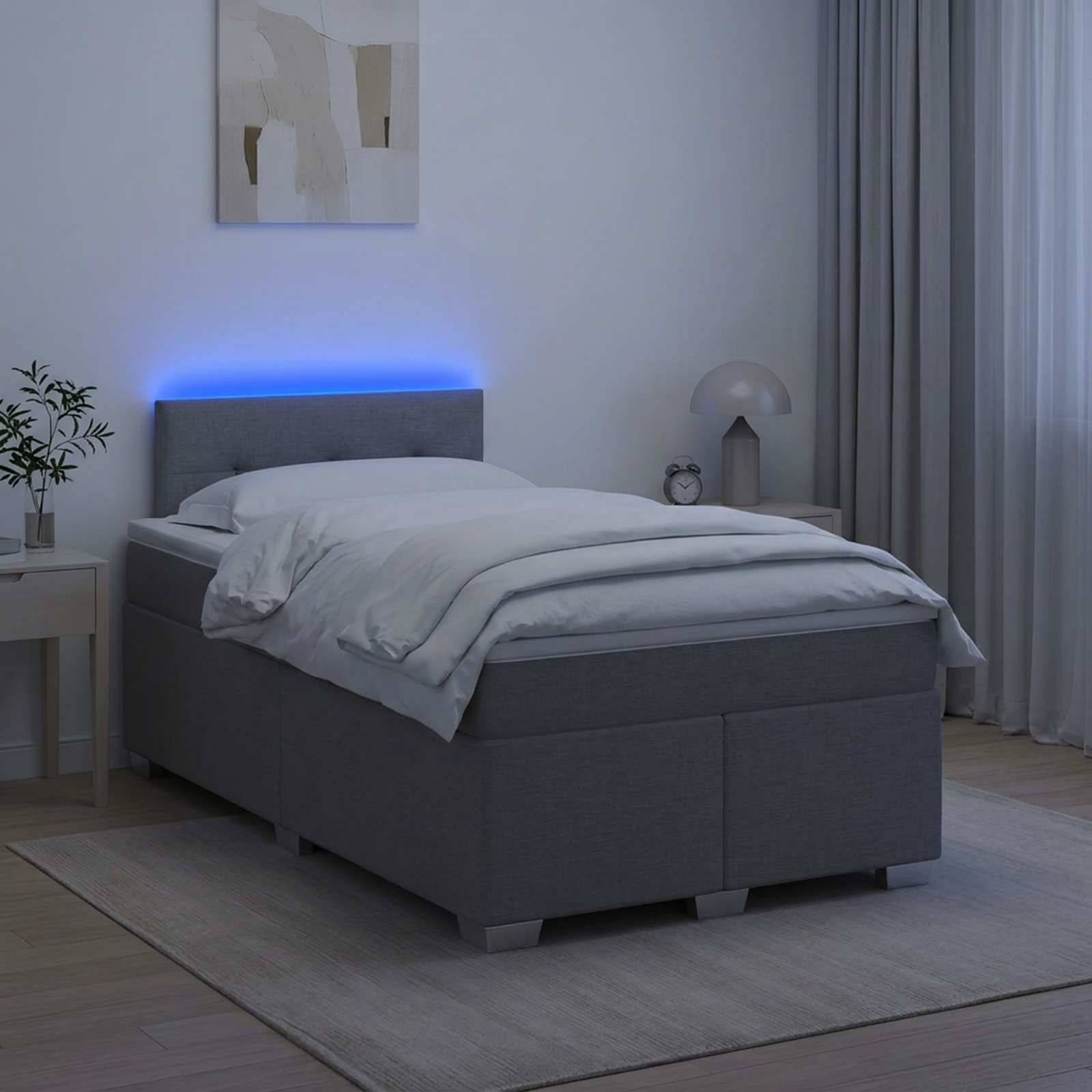 Modernes Schlafzimmer mit einem grau gepolsterten Bett, weißer Bettwäsche, blauem LED-Kopfleuchten-Glühen, Nachttisch, Lampe und Vorhängen in minimalistischer Inneneinrichtung.