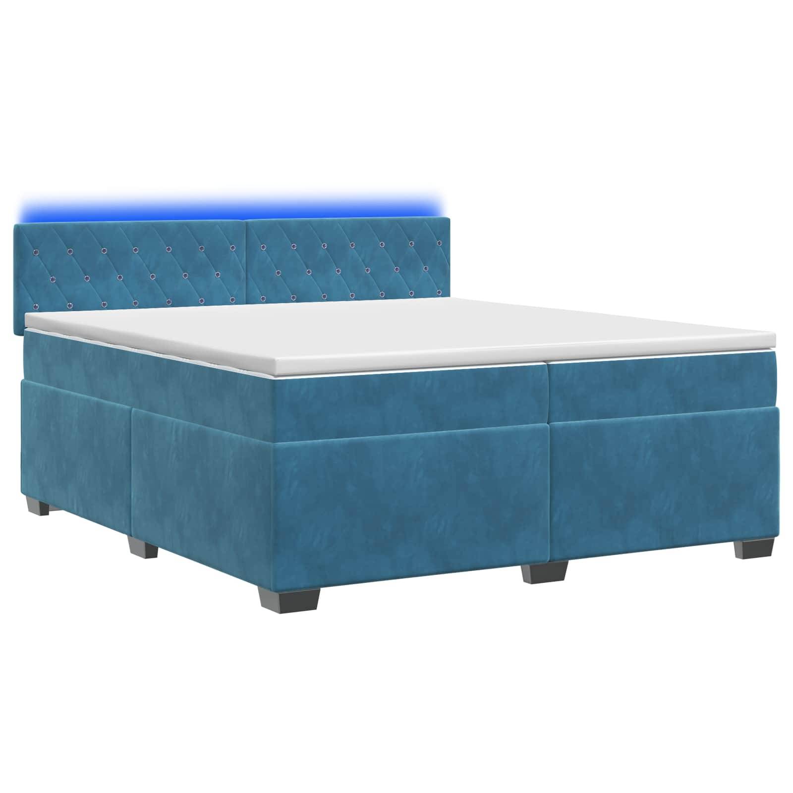 Bett mit blauem Polsterstoff, gestepptem Kopfteil und weißer Matratze vor neutralem Hintergrund.