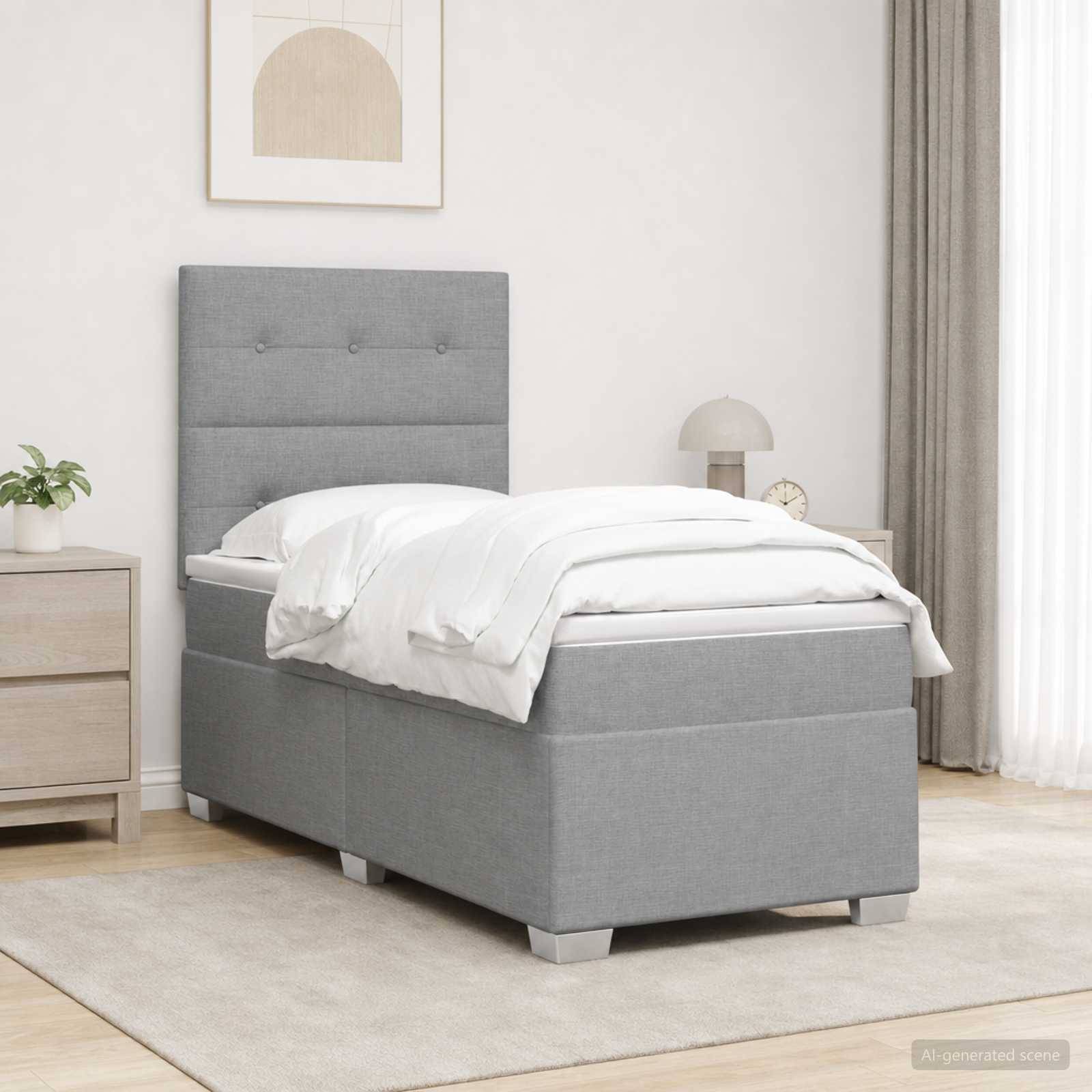 Graues, gepolstertes Einzelbett mit weißer Bettwäsche in einem minimalistischen Schlafzimmer, neben einem Nachttisch und einer Lampe, auf einem hellen Teppich.