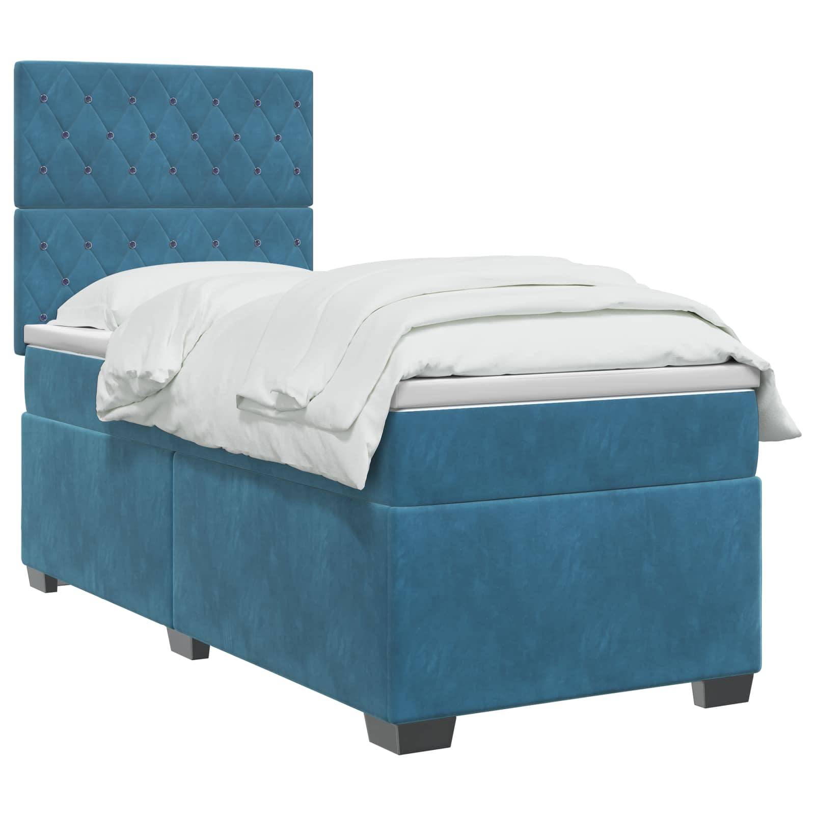 Blaugepolstertes Einzelbett mit gestepptem Kopfteil, weißer Bettwäsche und Stauraumbasis auf kurzen Beinen.
