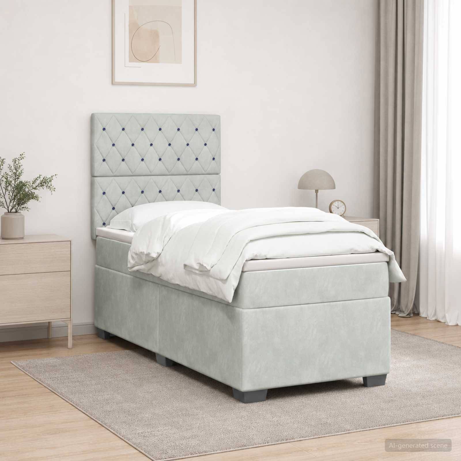 Ein hellgraues gepolstertes Einzelbett mit gestepptem Kopfteil, weißer Bettwäsche und passendem Stauraum-Bettkasten in einem minimalistischen Schlafzimmer mit Teppich, Nachttisch, Lampe und Vorhängen.