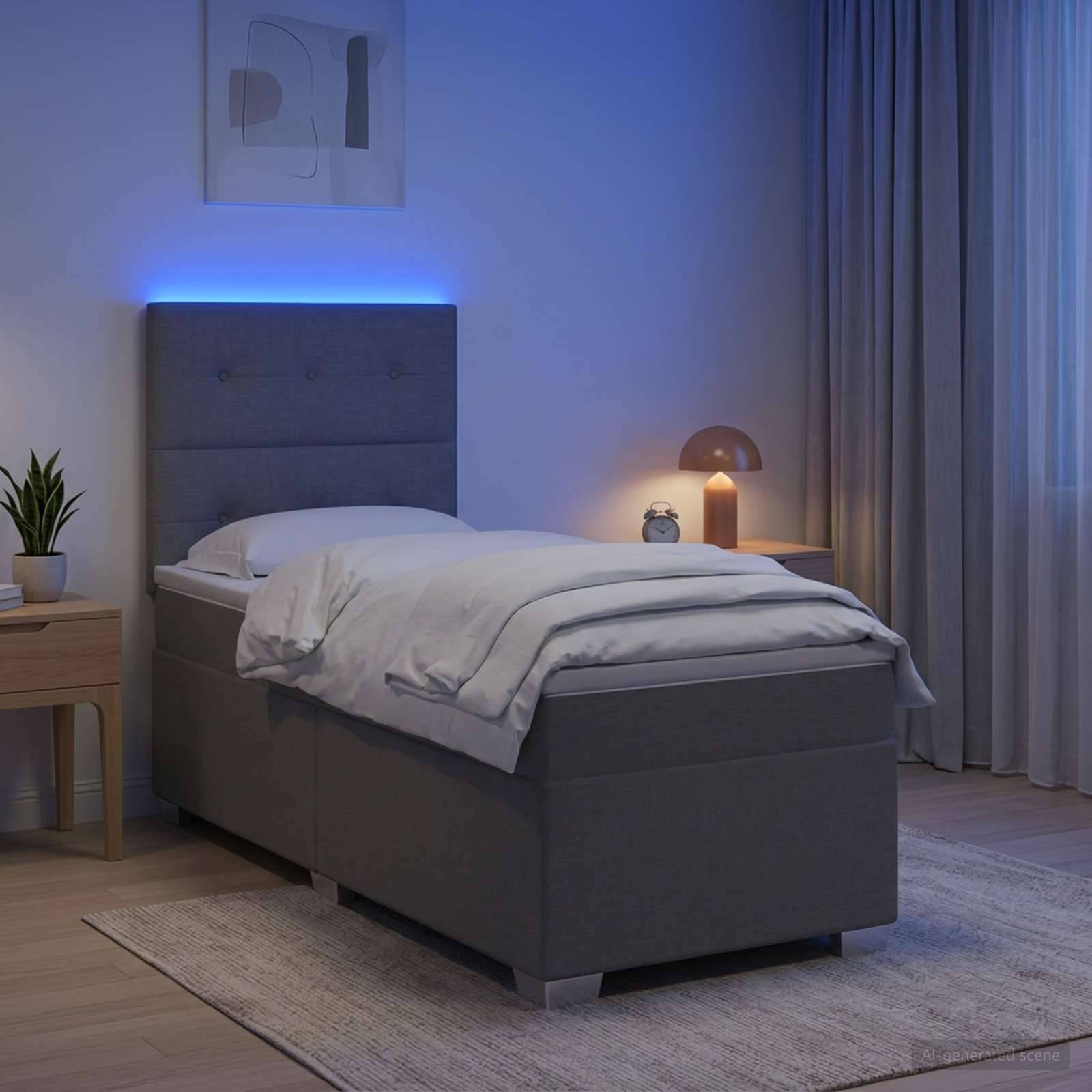 Modernes graues Einzelbett mit weißer Bettwäsche in einem sanft beleuchteten Schlafzimmer mit blauer Kopfleuchte, einer Nachttischlampe, Vorhängen, Teppich und einer kleinen Pflanze.