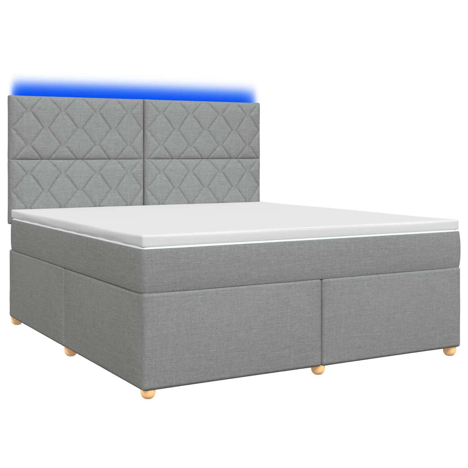 Grau gepolstertes Bett mit gestepptem Kopfteil und blau beleuchteter oberer Kante, zeigt eine Matratze auf einem Boxspring vor weißem Hintergrund.