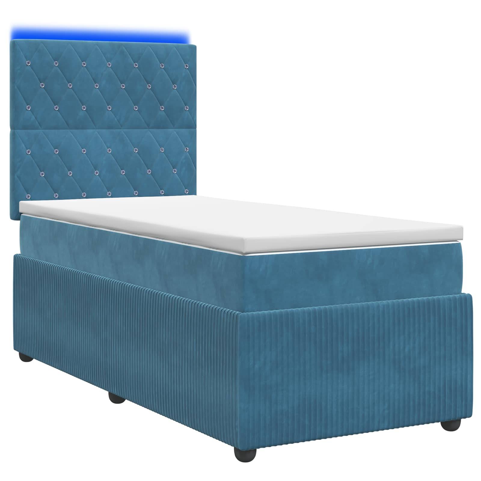Einzelbett mit blauem Polsterstoff, gestepptem Kopfteil und weißer Matratze vor einfarbigem Hintergrund.