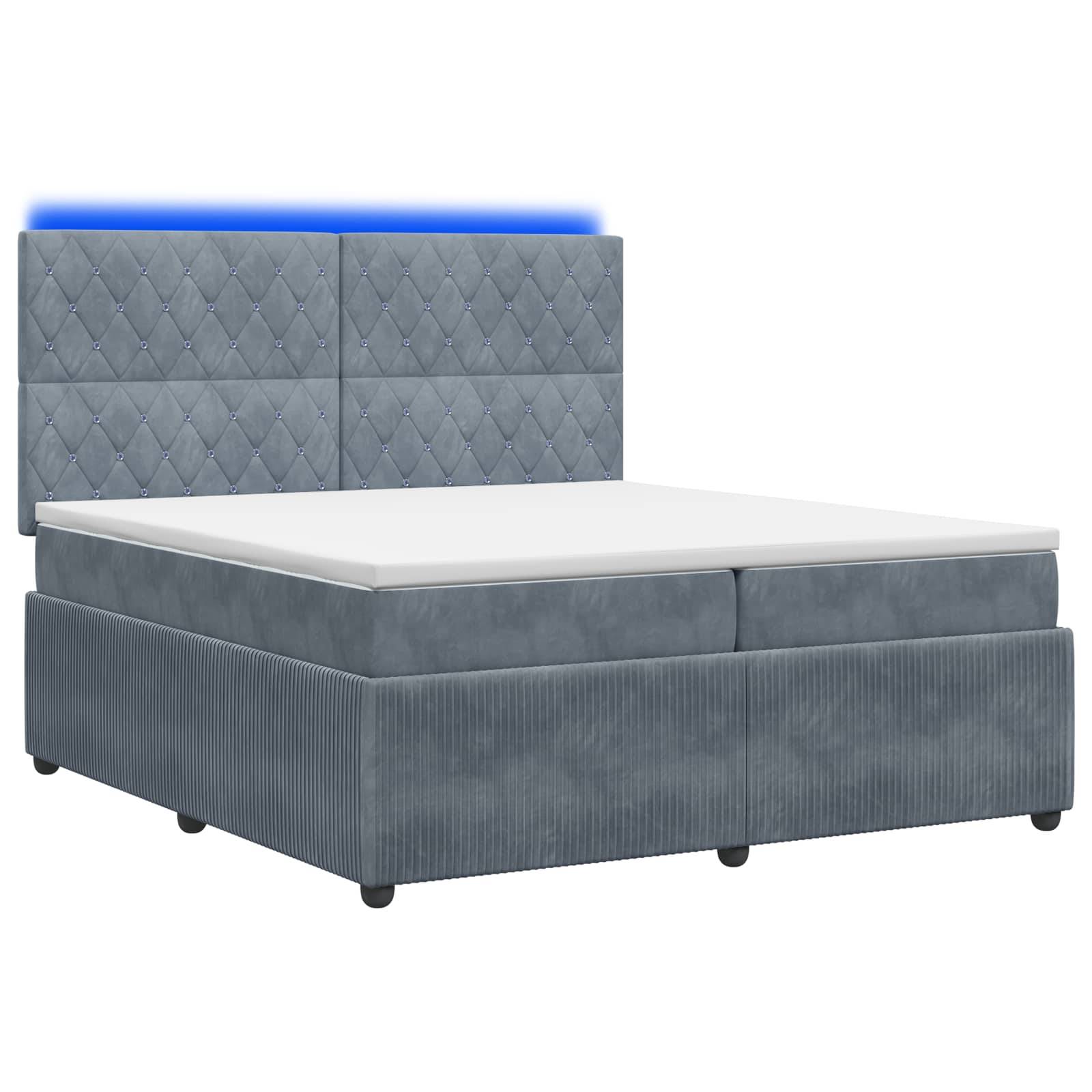 Grau gepolstertes Bett mit hohem gestepptem Kopfteil und weißer Matratze auf einfacher Boxspring-Basis.