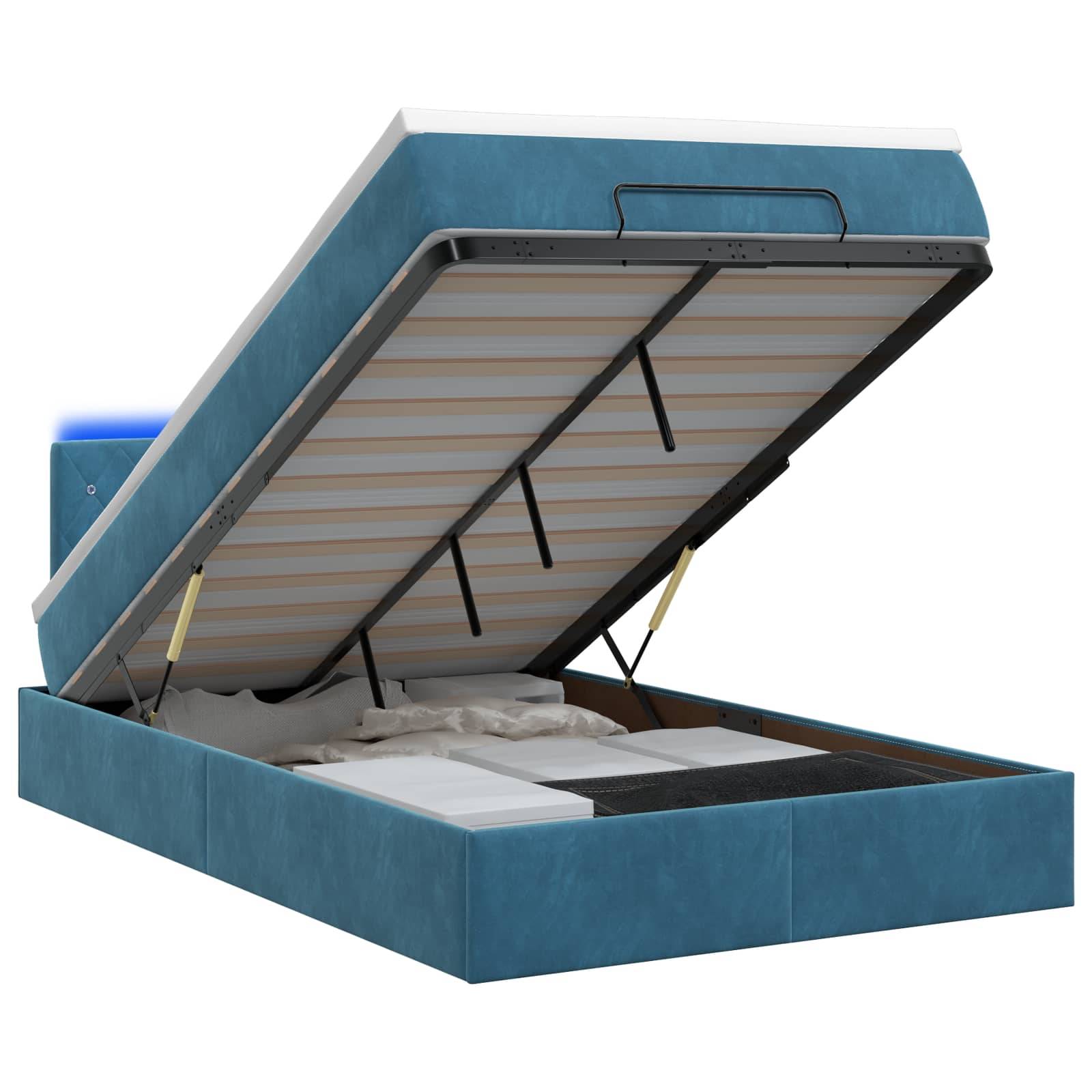 Blaugepolstertes Speicherbett mit Matratzenplattform, die auf hydraulischen Stützen hochgeklappt ist und das Unter-Bett-Fach offenbart.