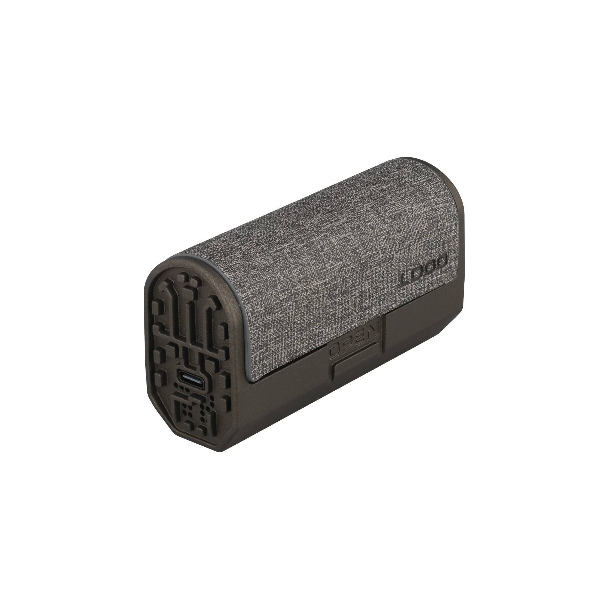 Tragbarer Bluetooth-Lautsprecher mit grauem Stoffüberzug, schwarzer Endkappe und sichtbarem USB-Ladeanschluss auf weißem Hintergrund.