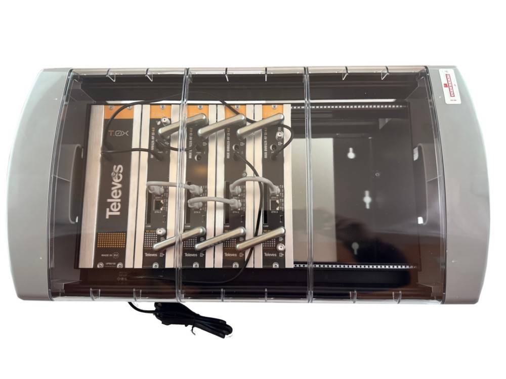 Ein wandmontierter Televés Fernseh-/Rundfunkverteilverstärker in einem transparenten Schutzgehäuse mit sichtbaren Koaxialverbindungen und Stromkabel.