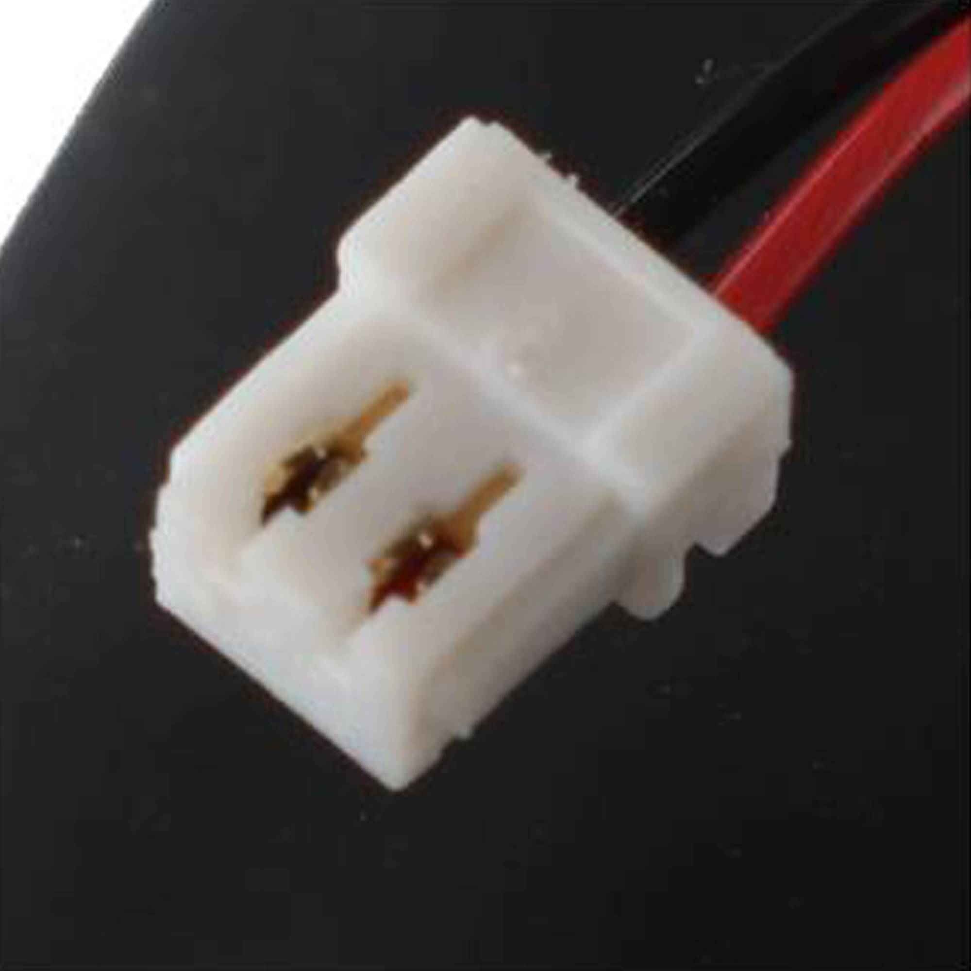 Nahaufnahme eines weißen zweipoligen Elektroanschlusses mit roten Kabeln auf dunklem Hintergrund.