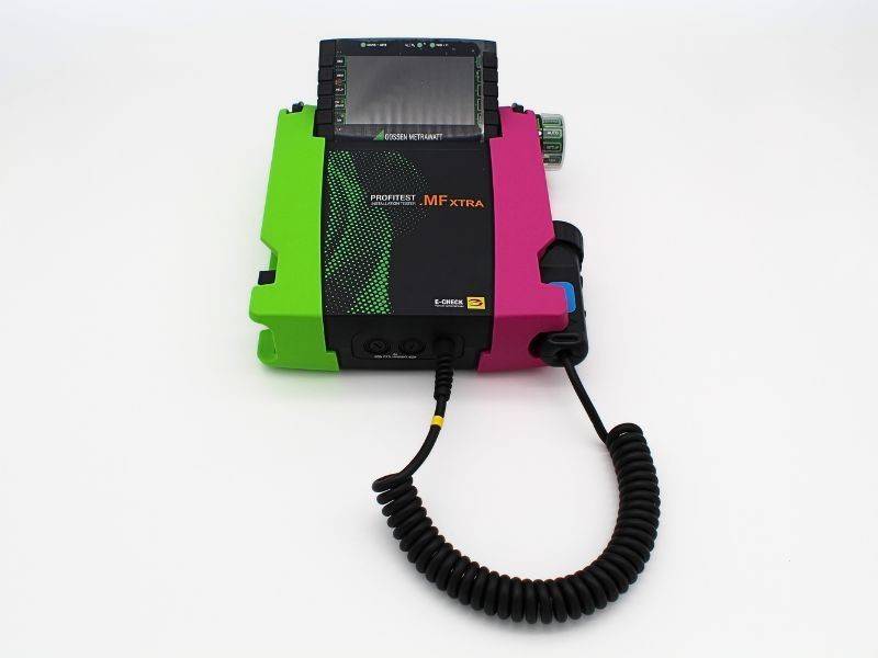 Tragbares, tragbares Monitor-/Defibrillator-Gerät auf weißem Hintergrund, mit grünem und magentafarbenem Gehäuse, Bildschirm oben und angebrachten spiralförmigen Kabeln.