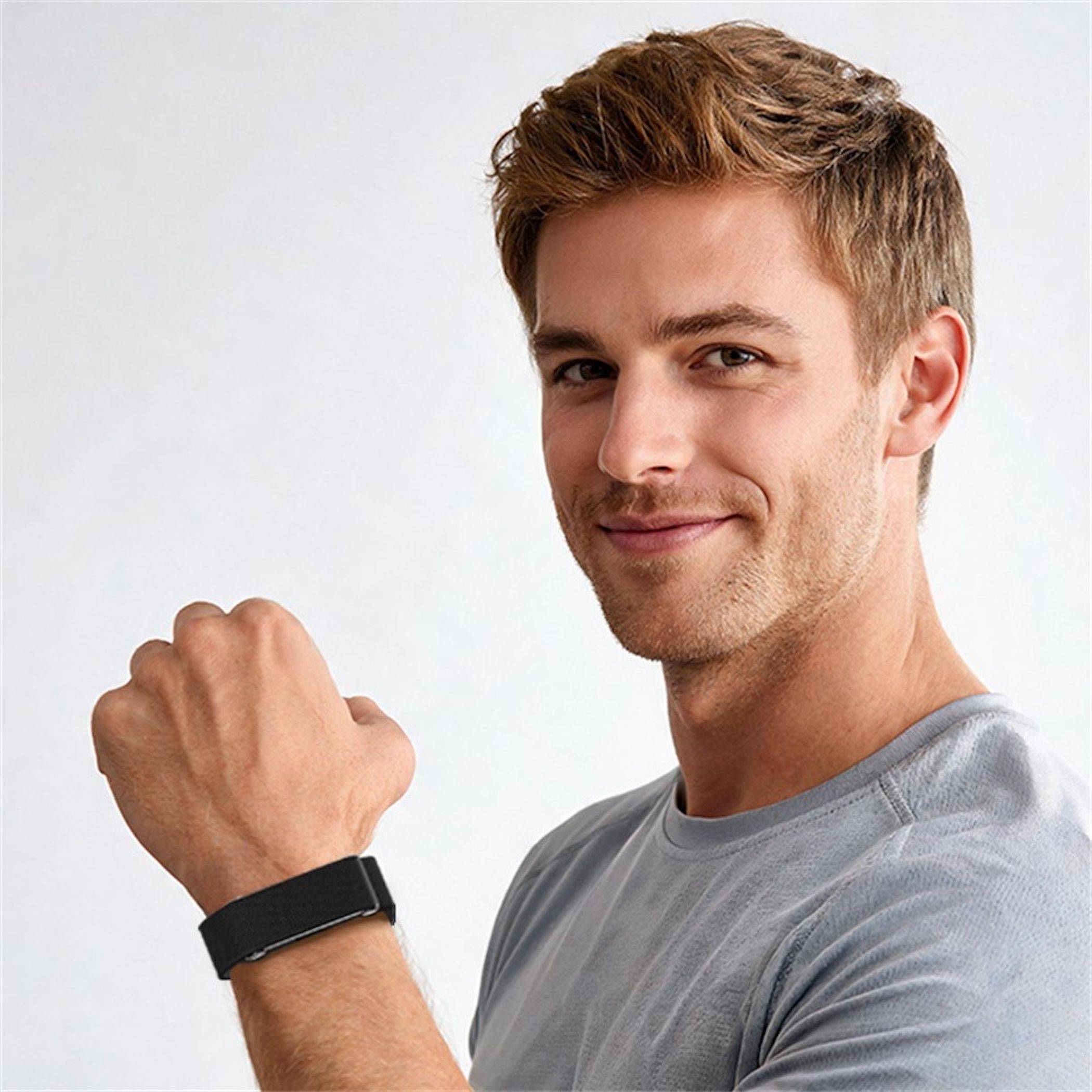Lächelnder Mann im grauen Hemd, der eine schwarze Fitness-Uhr an seinem Handgelenk vor einem einfachen weißen Hintergrund zeigt.