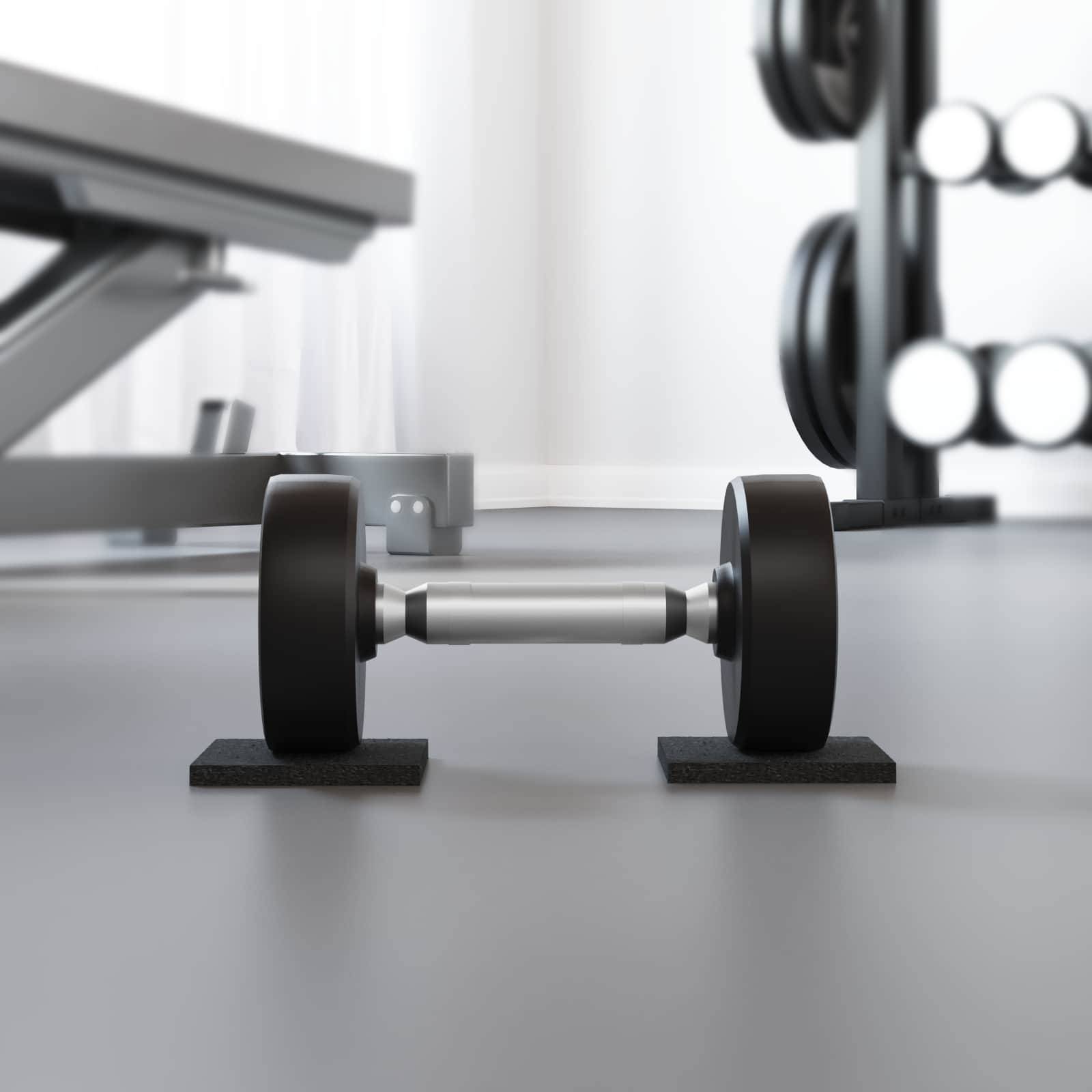 Einzelne Hantel, die auf dem Boden eines Fitnessstudios neben einer Bank und einem Rack in einem hell erleuchteten Fitnessraum liegt.