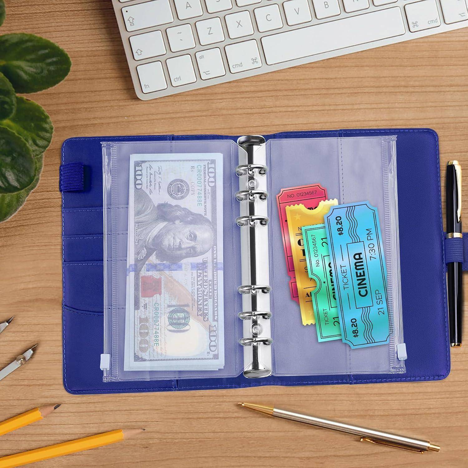 Offener blauer Ordner mit einer Geldtasche voller 100-Dollar-Scheine und farbenfrohen Kinokarten auf einem Schreibtisch neben einer Tastatur und einem Stift.