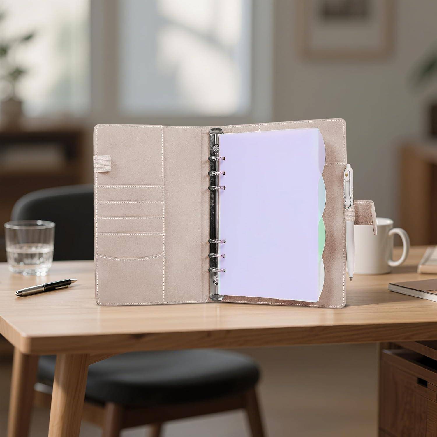 Offener beiger Ringordner-Planer auf einem Schreibtisch, mit sichtbaren farbigen Registerreitern und einem Stift daneben in einer Home-Office-Umgebung.
